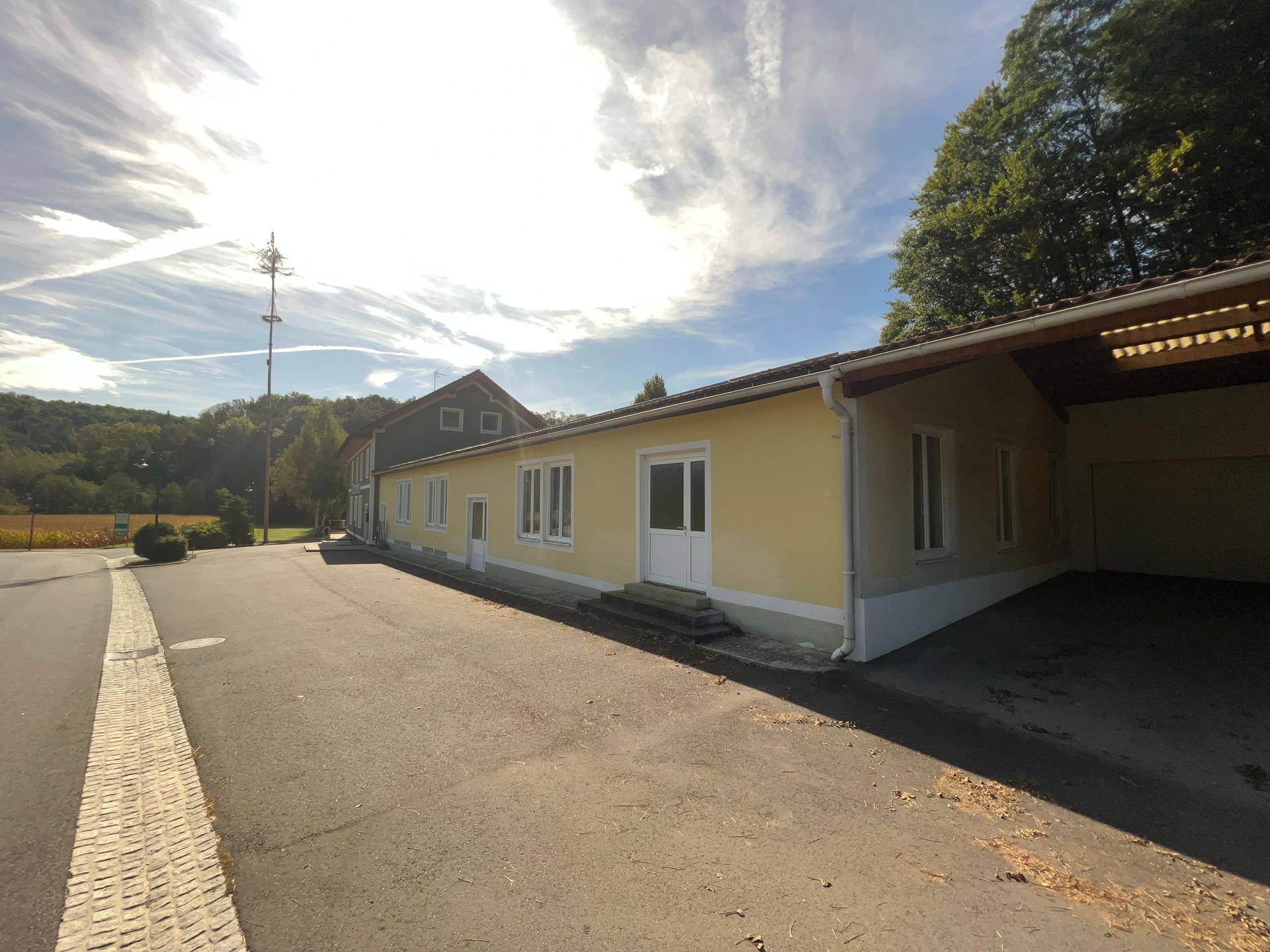 Seitenansicht des Hauptgebäudes und des gelben Anbaus mit angrenzendem Carportbereich.