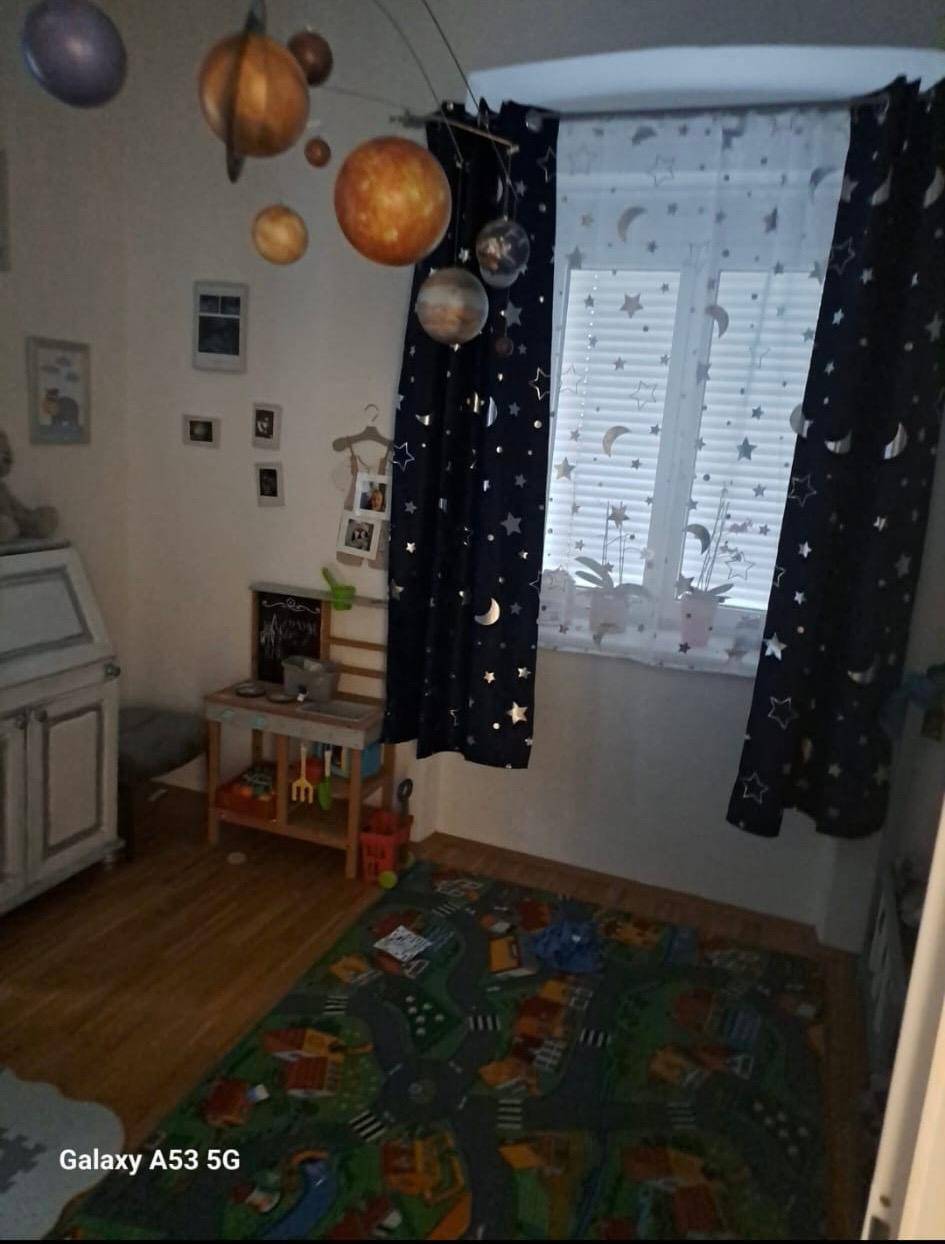 Kinderzimmer mit spielerischem Teppich, Planeten-Dekoration und Vorhängen mit Sternenmuster am Fenster.