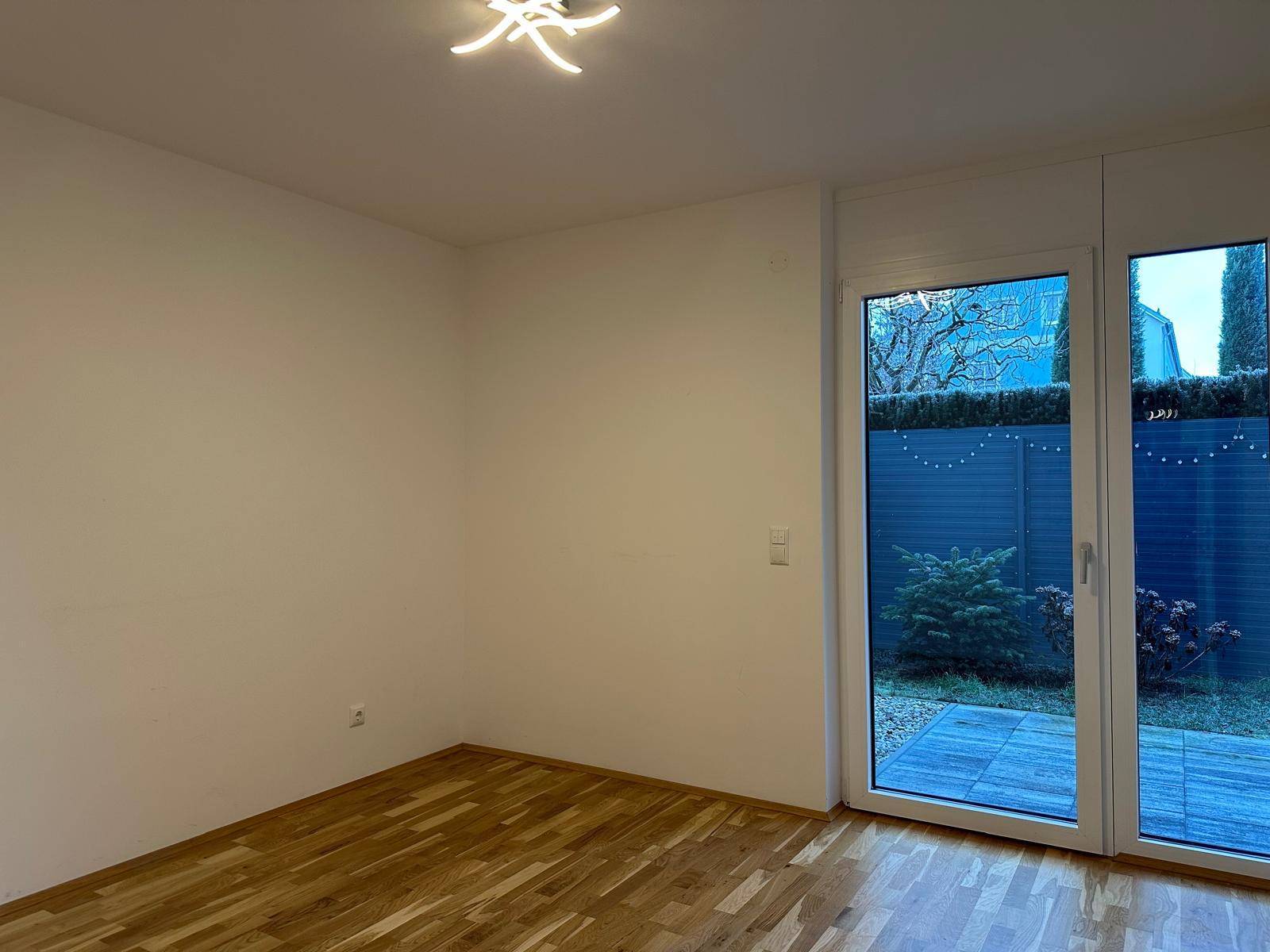 Heller Wohnraum mit Holzboden und breiten Fenstertüren, die viel Tageslicht hereinlassen.