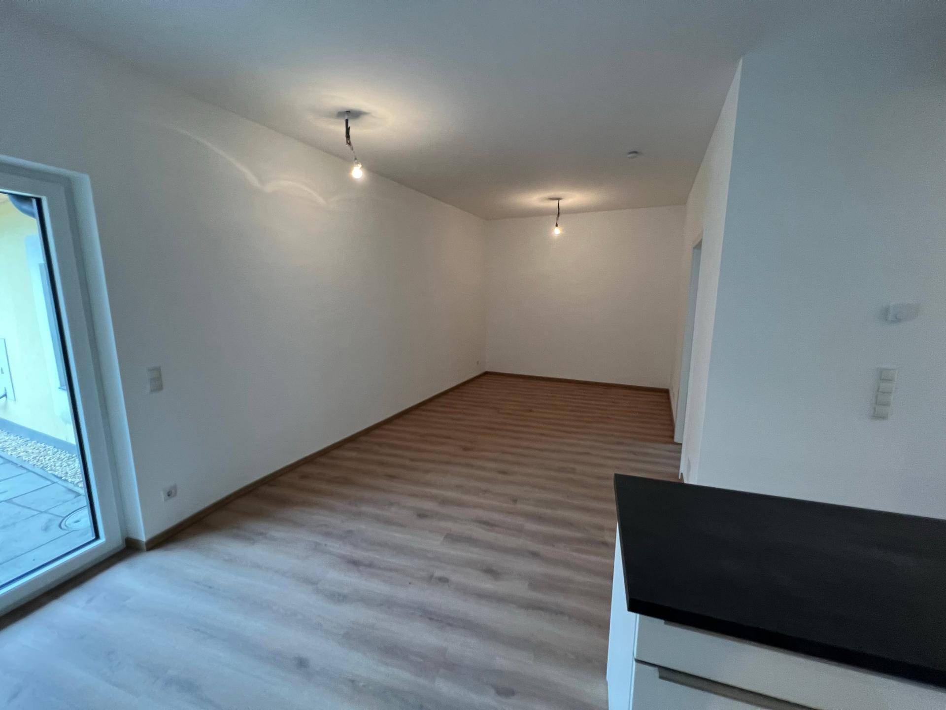 Helles, leeres Zimmer mit Laminatboden und großen Fenstern, bereit zur individuellen Einrichtung.