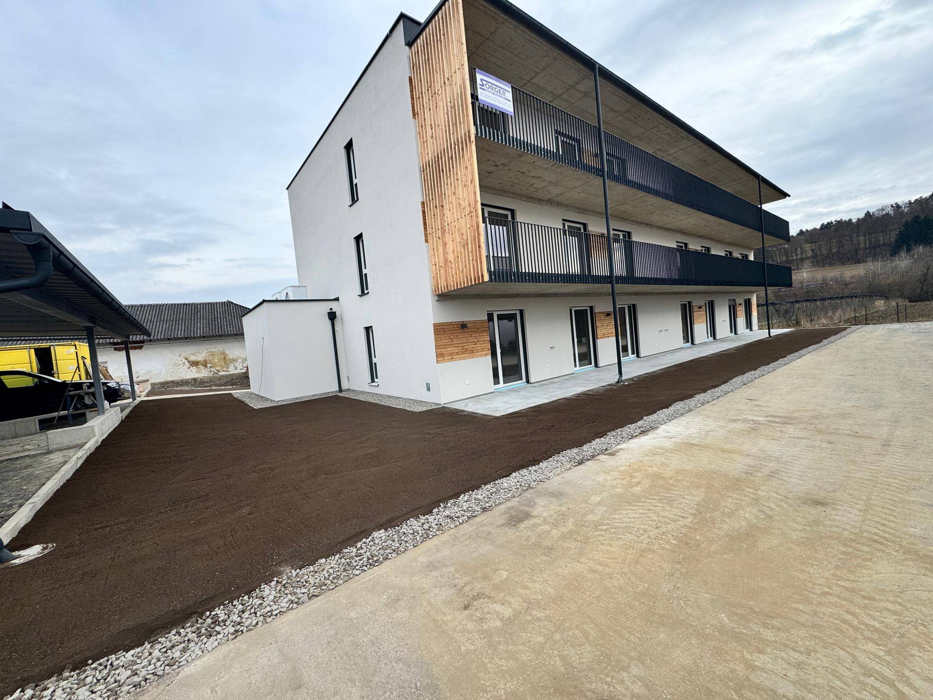Neubau-Mehrfamilienhaus mit moderner Architektur, Balkonen und angrenzendem Parkplatzbereich mit Carport.