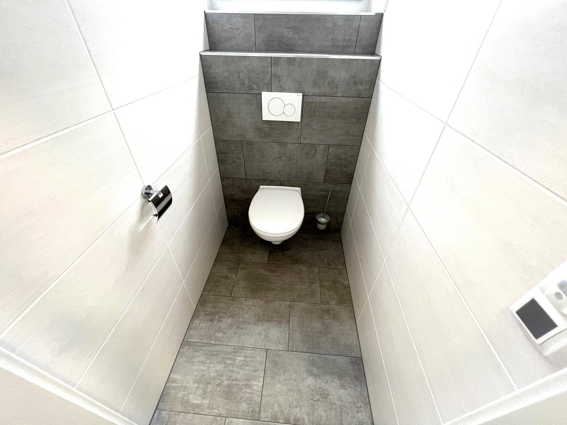 Sauberes und modernes WC mit Wand-WC und grauen Bodenfliesen, in einwandfreiem Zustand.