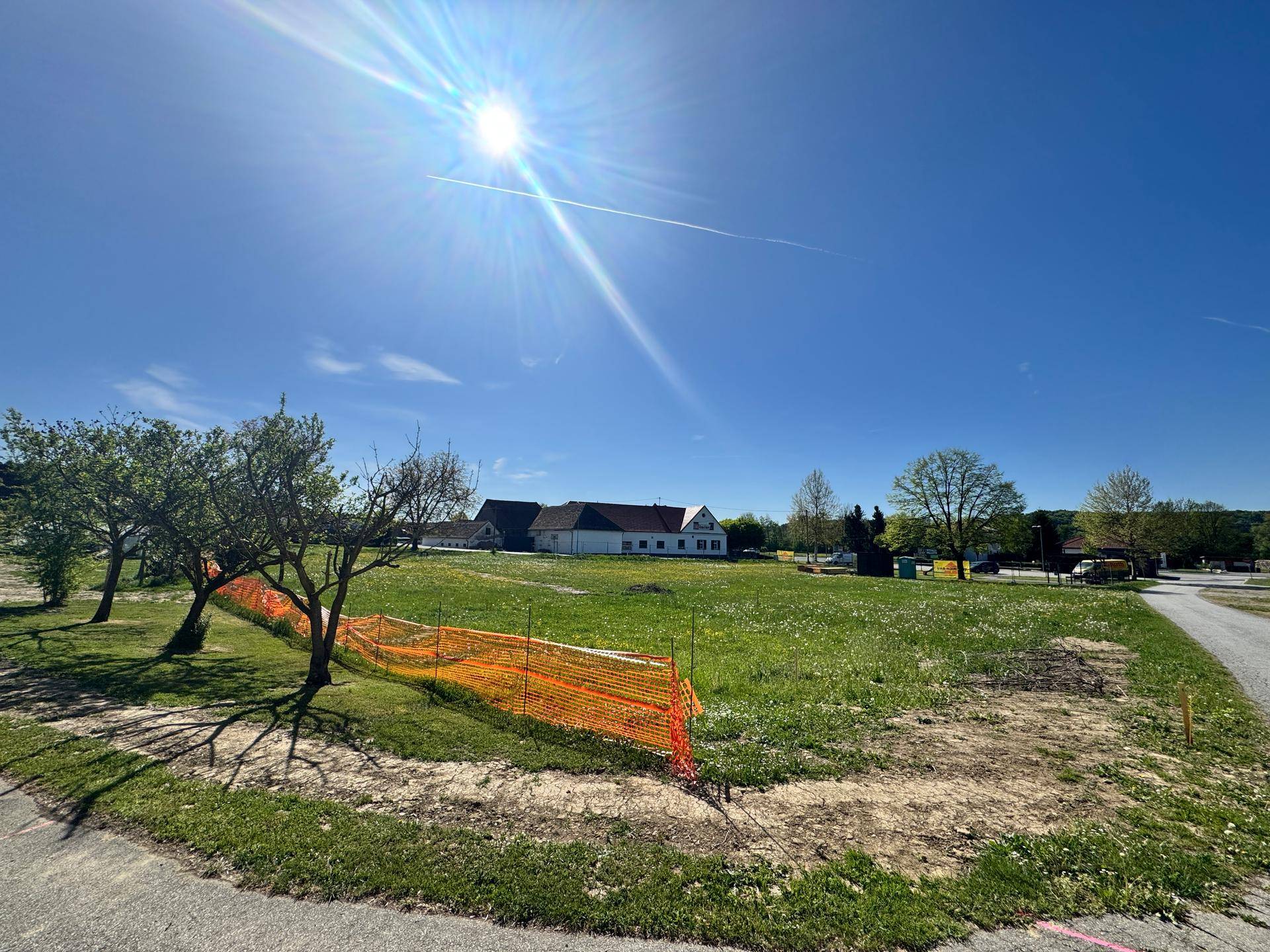 Sonniges, offenes Grundstück mit grüner Wiese, Bäumen und Blick auf die umliegende Landschaft.