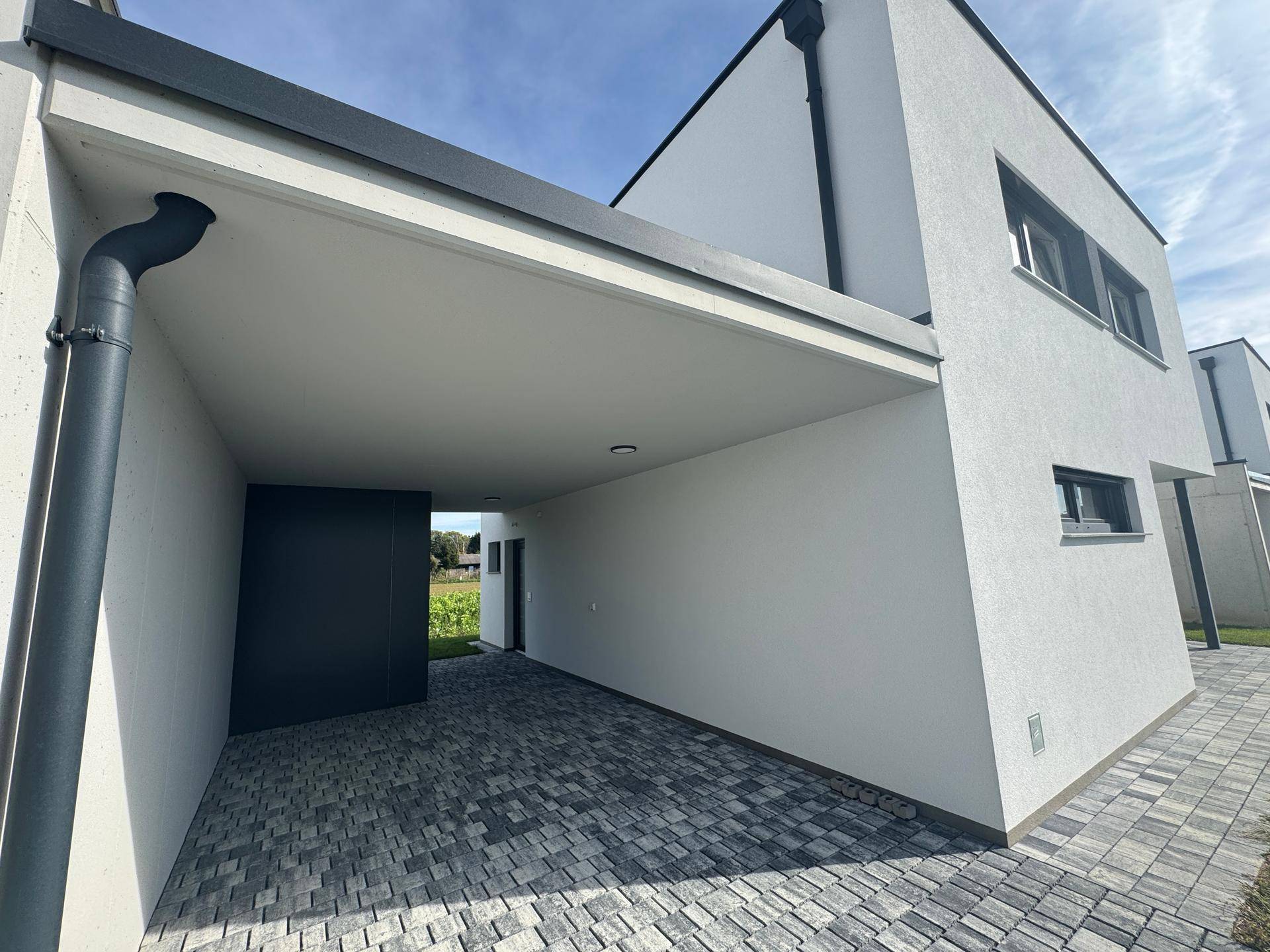 Moderne Hausfassade mit Carport und gepflasterter Zufahrt.