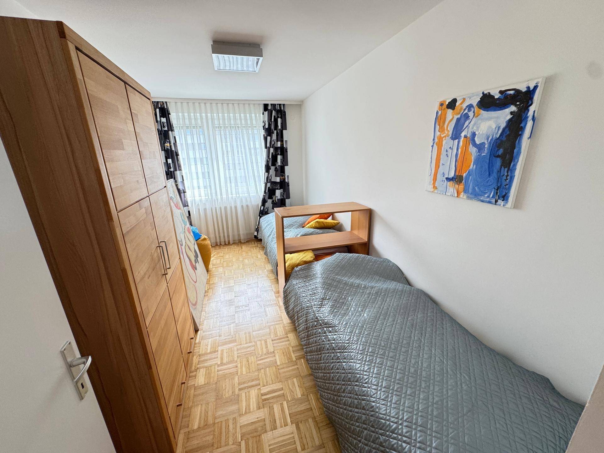 Kinder- oder Gästezimmer mit zwei Einzelbetten, Holzschrank und Parkettboden.