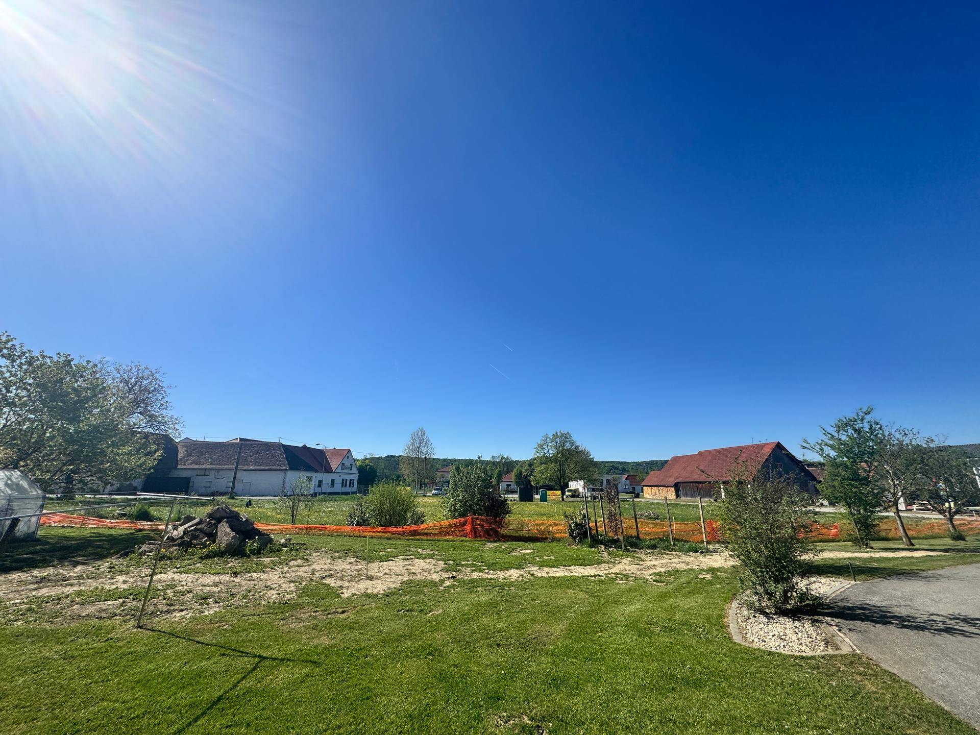 Weitläufiges Grundstück mit grüner Vegetation und traditionellen Gebäuden im Hintergrund unter hellem Sonnenlicht.