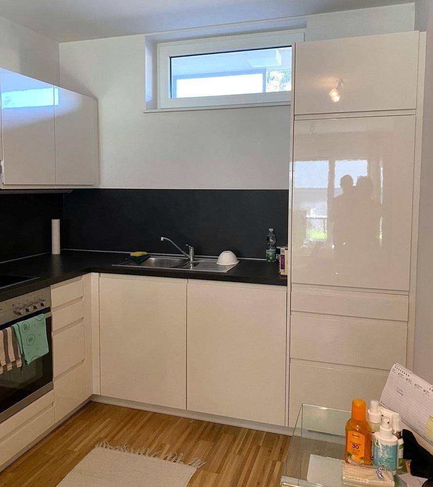 Helle Küche mit weißen Hochglanzschränken, Spüle und Fenster.