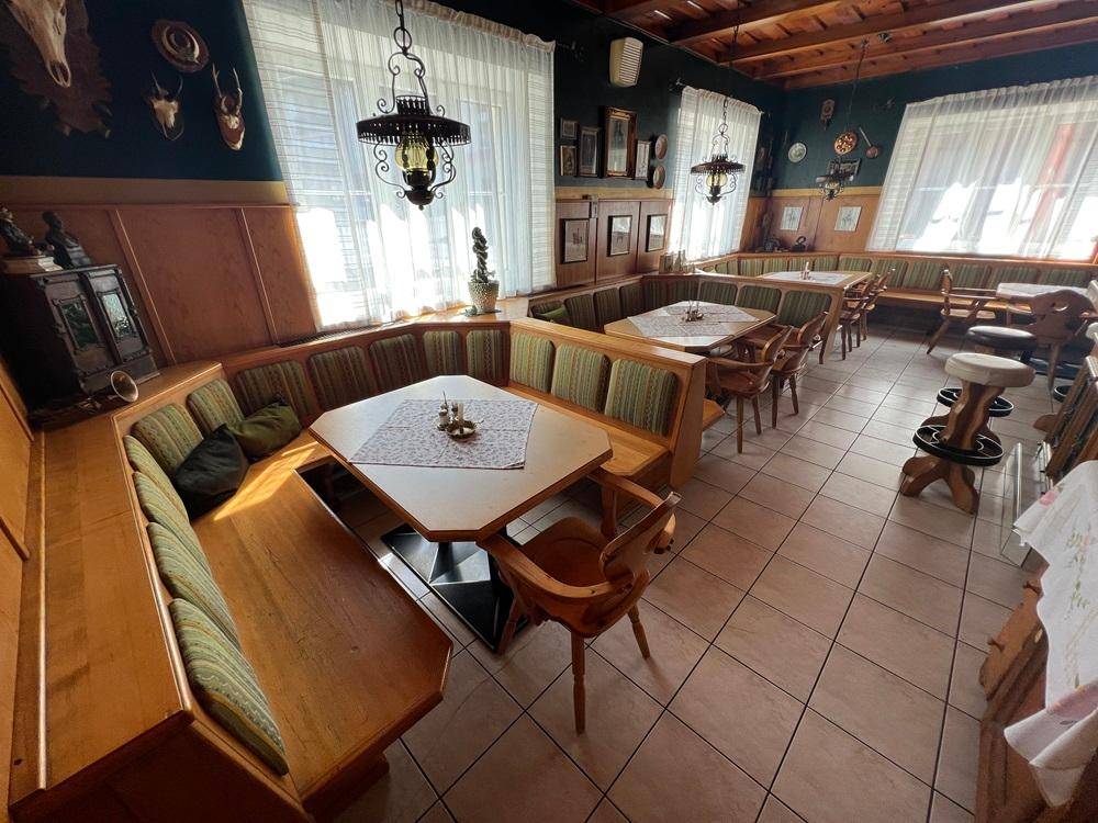 Gemütlicher Restaurantbereich mit traditionellen Holzbänken, Tischen und rustikalen Deckenleuchten.