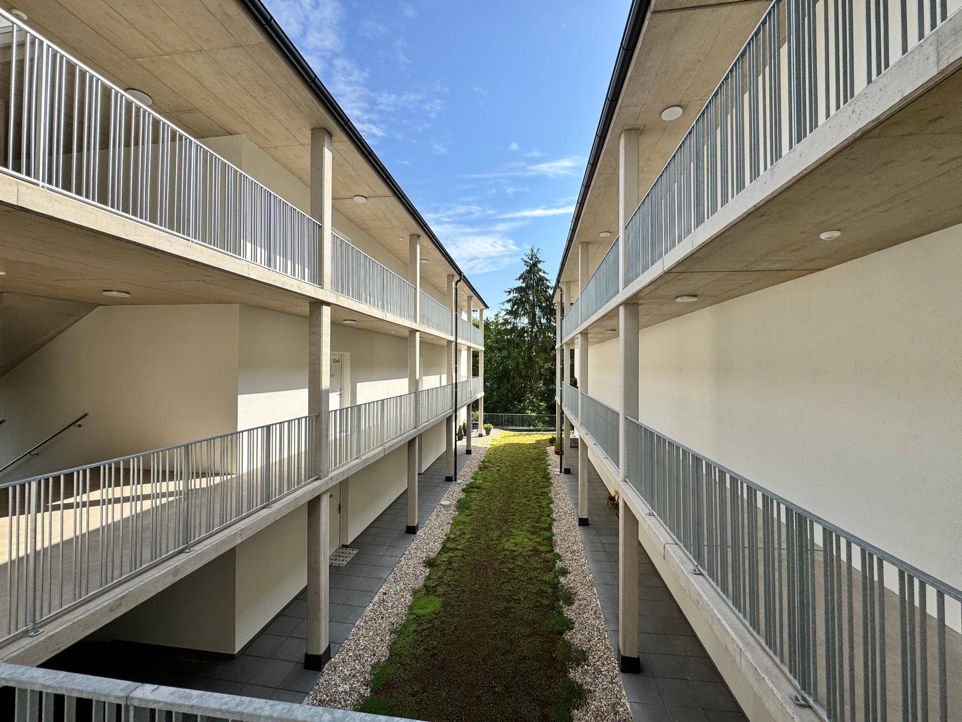 Innenhof eines modernen Wohnkomplexes mit begrüntem Mittelstreifen und Balkonen.