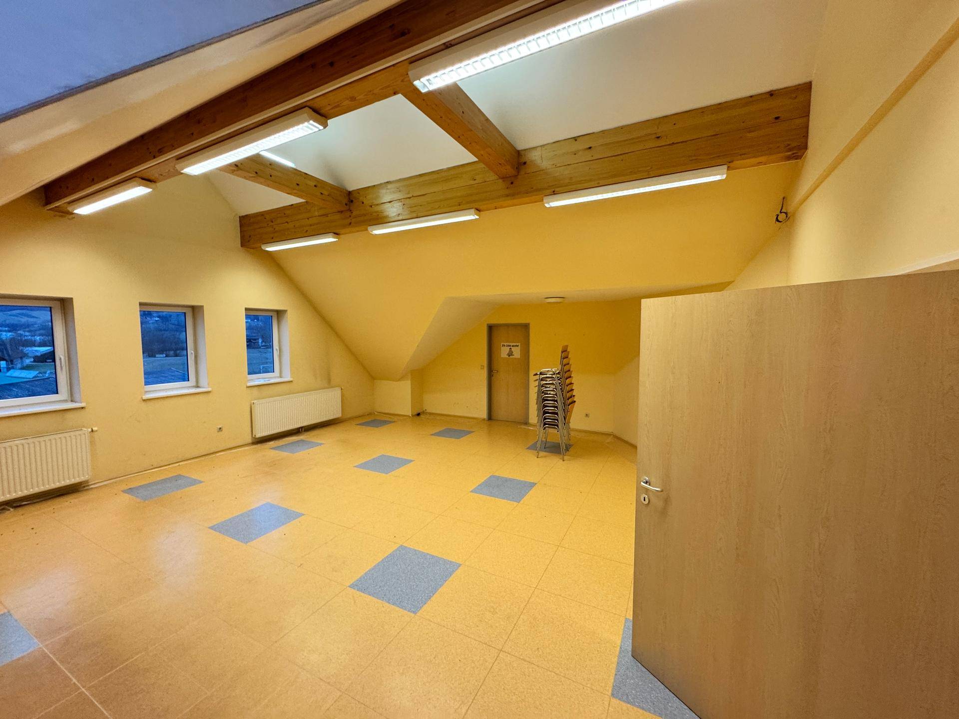 Heller Dachbodenraum mit schrägen Wänden, farbigem Boden und Deckenbeleuchtung.