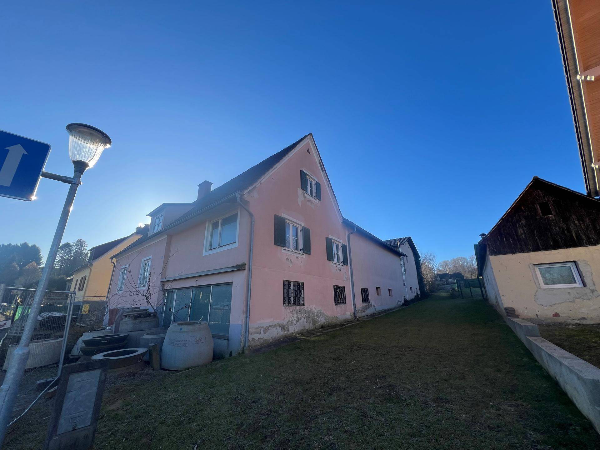 Seitenansicht des rosa Hauses mit angrenzendem Nebengebäude und einem Hang im Hintergrund.