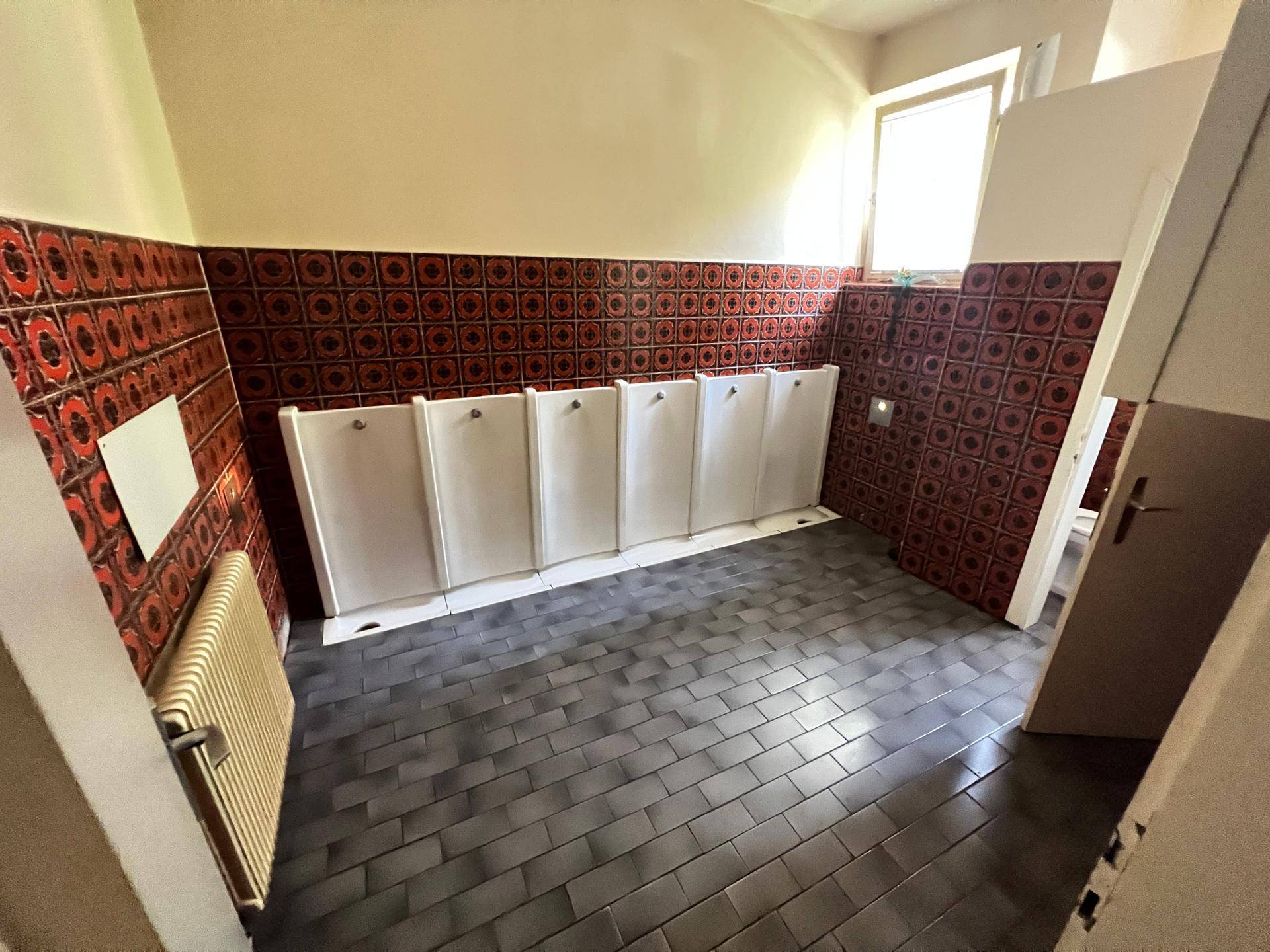 Herren-WC mit Urinalen, gemusterten roten Fliesen und einem Fenster.
