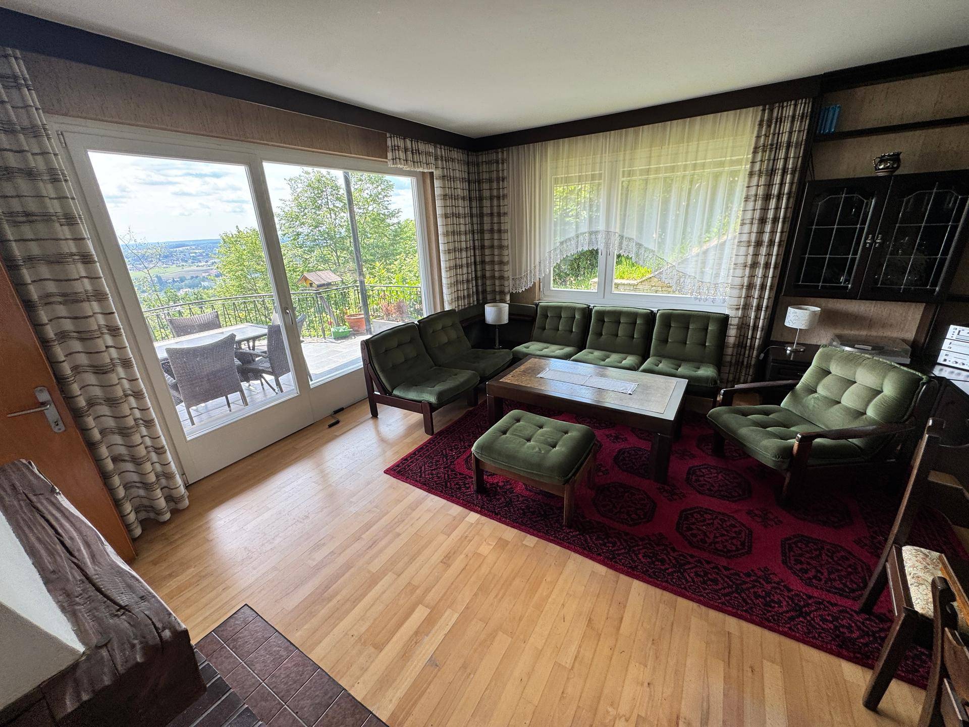 Gemütliches Wohnzimmer mit Holzboden, grünen Sofas und großem Fenster mit Weitblick.