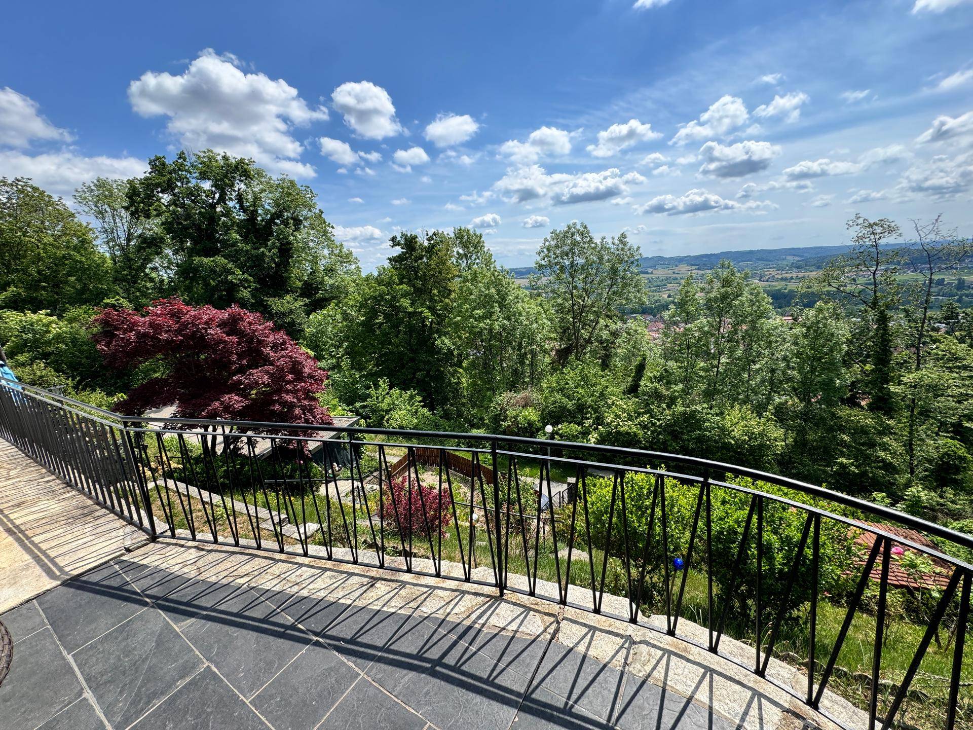 Blick vom Balkon mit schmiedeeisernem Geländer auf die weite, grüne Landschaft und den Horizont.