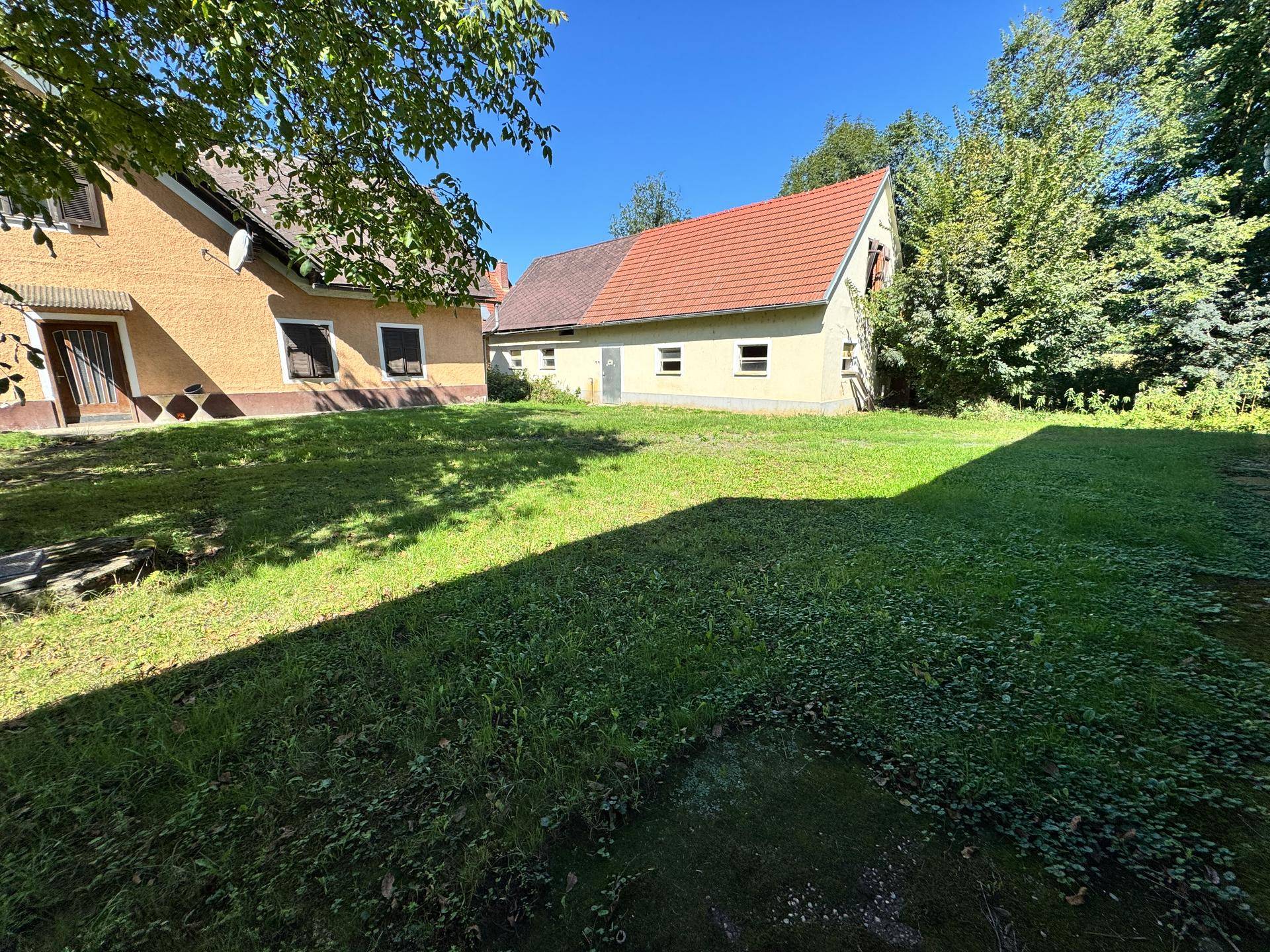 Große, gepflegte Rasenfläche vor dem Haus mit weiteren Gebäuden im Hintergrund an einem sonnigen Tag.