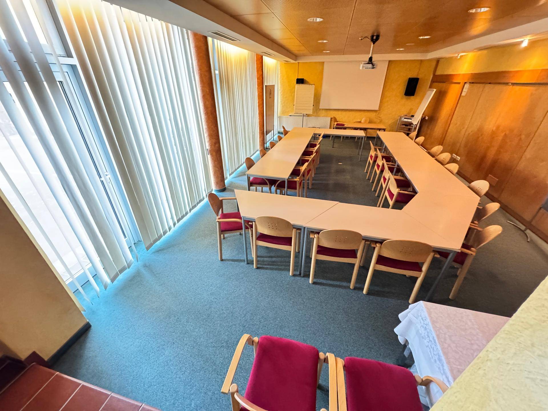 Konferenzraum mit U-förmiger Tischordnung, Teppichboden und großen Fenstern.