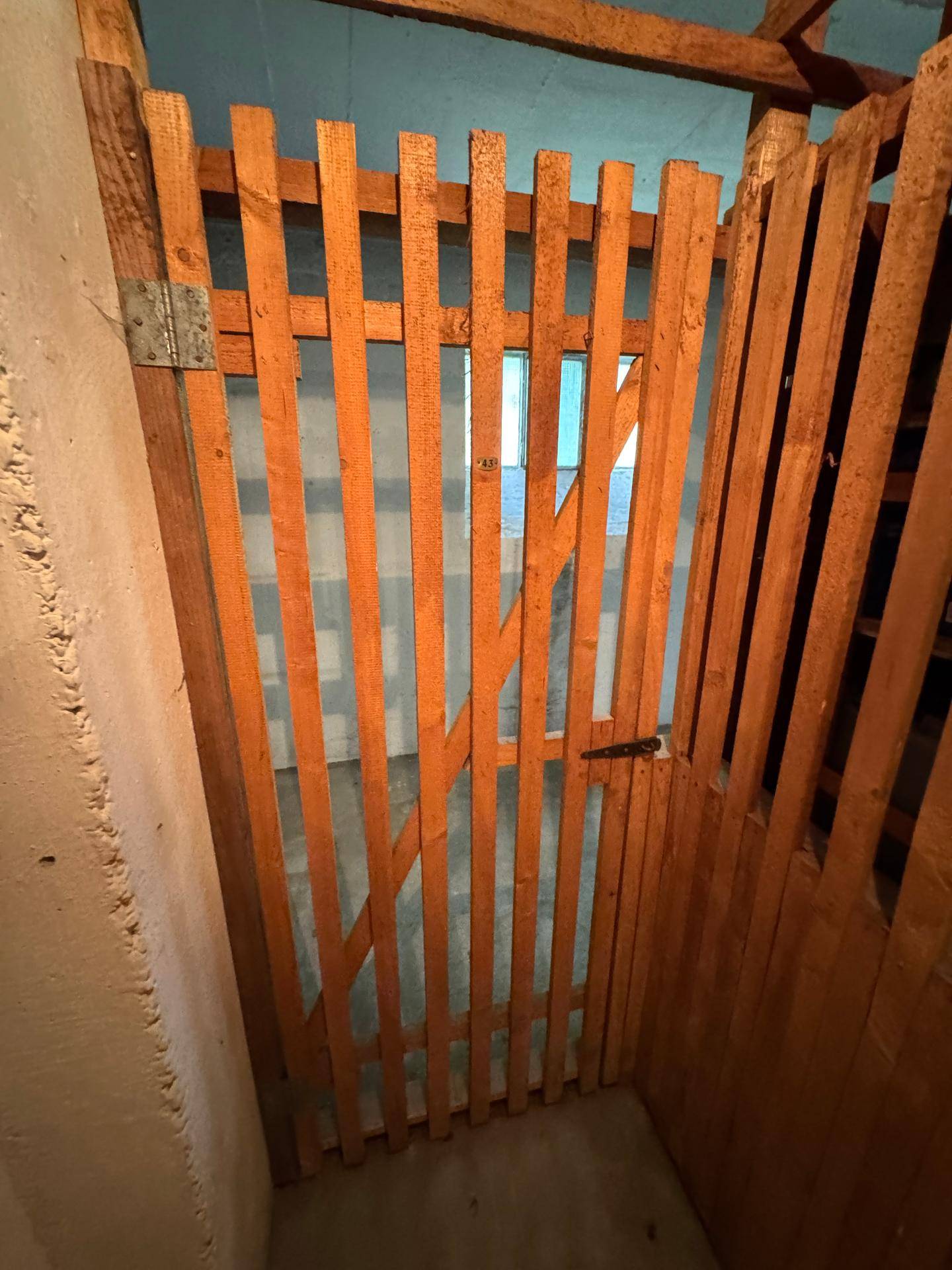 Holztür zu einem Lagerabteil in einem Keller oder Dachbodenbereich mit sichtbaren Holzbalken.