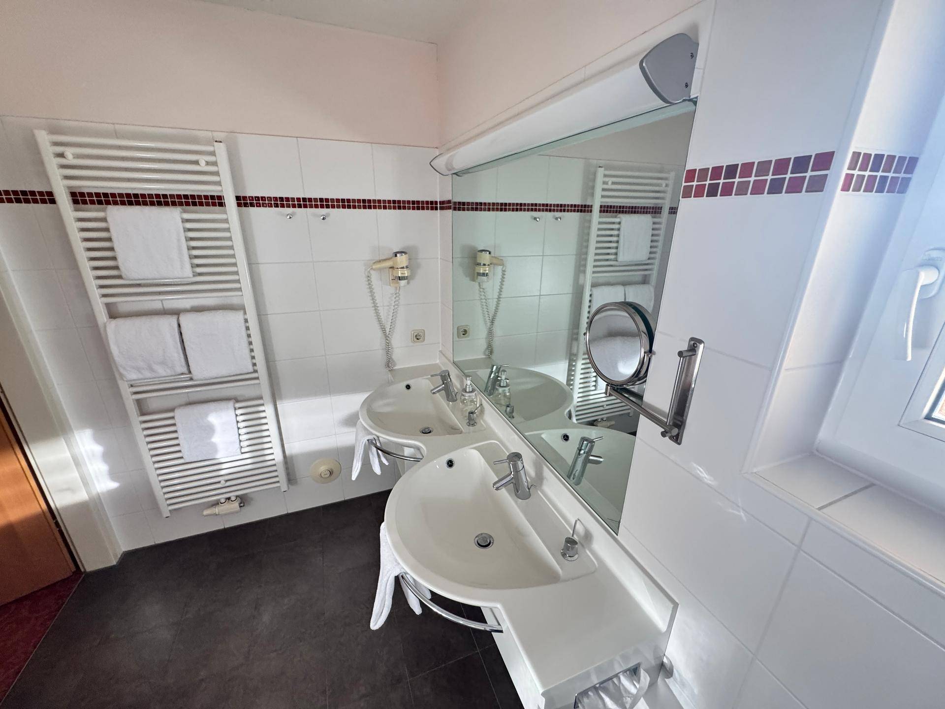Badezimmer mit Doppelwaschbecken, beheiztem Handtuchhalter und Spiegel.