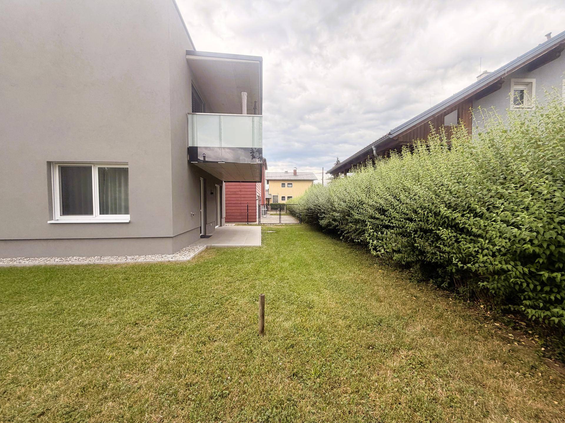 Seitenansicht des Gebäudes mit Balkon und angrenzendem Gartenbereich.