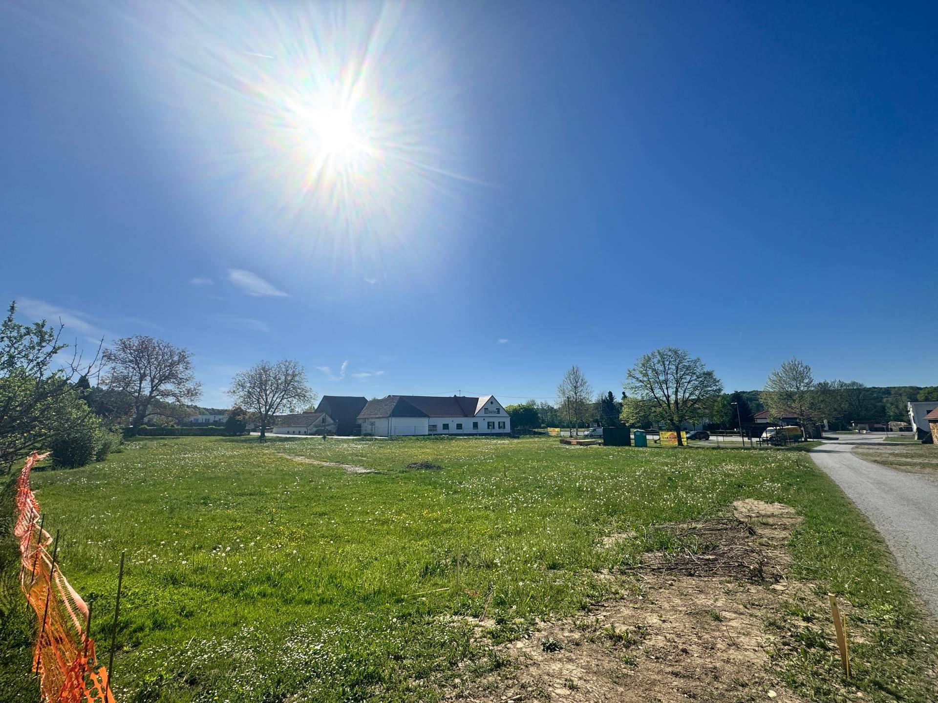 Weitläufiges grünes Grundstück unter strahlend blauem Himmel mit ländlicher Bebauung in der Ferne.