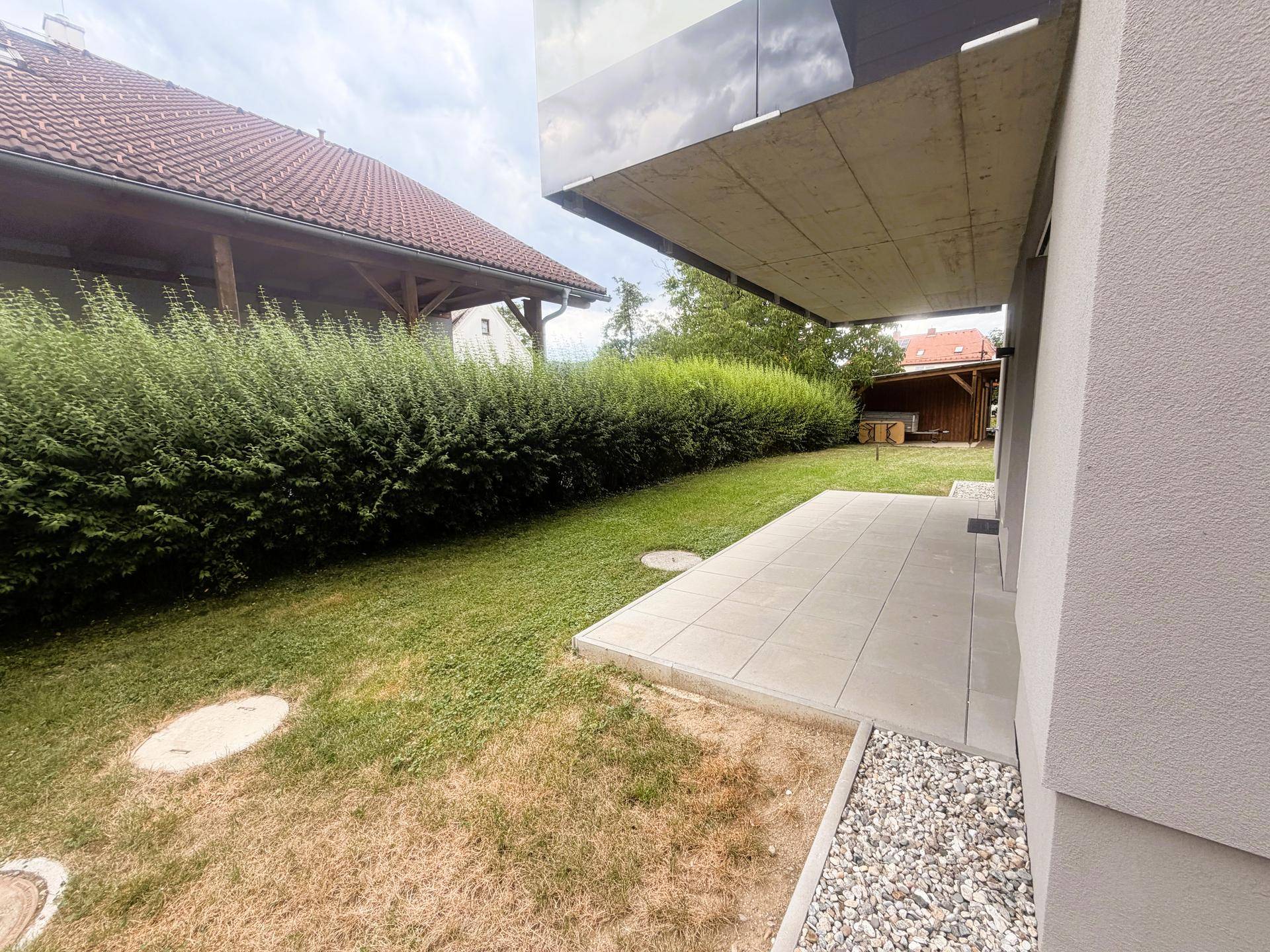 Seitlicher Gartenbereich mit Rasen und einer dichten Hecke entlang der Grundstücksgrenze.