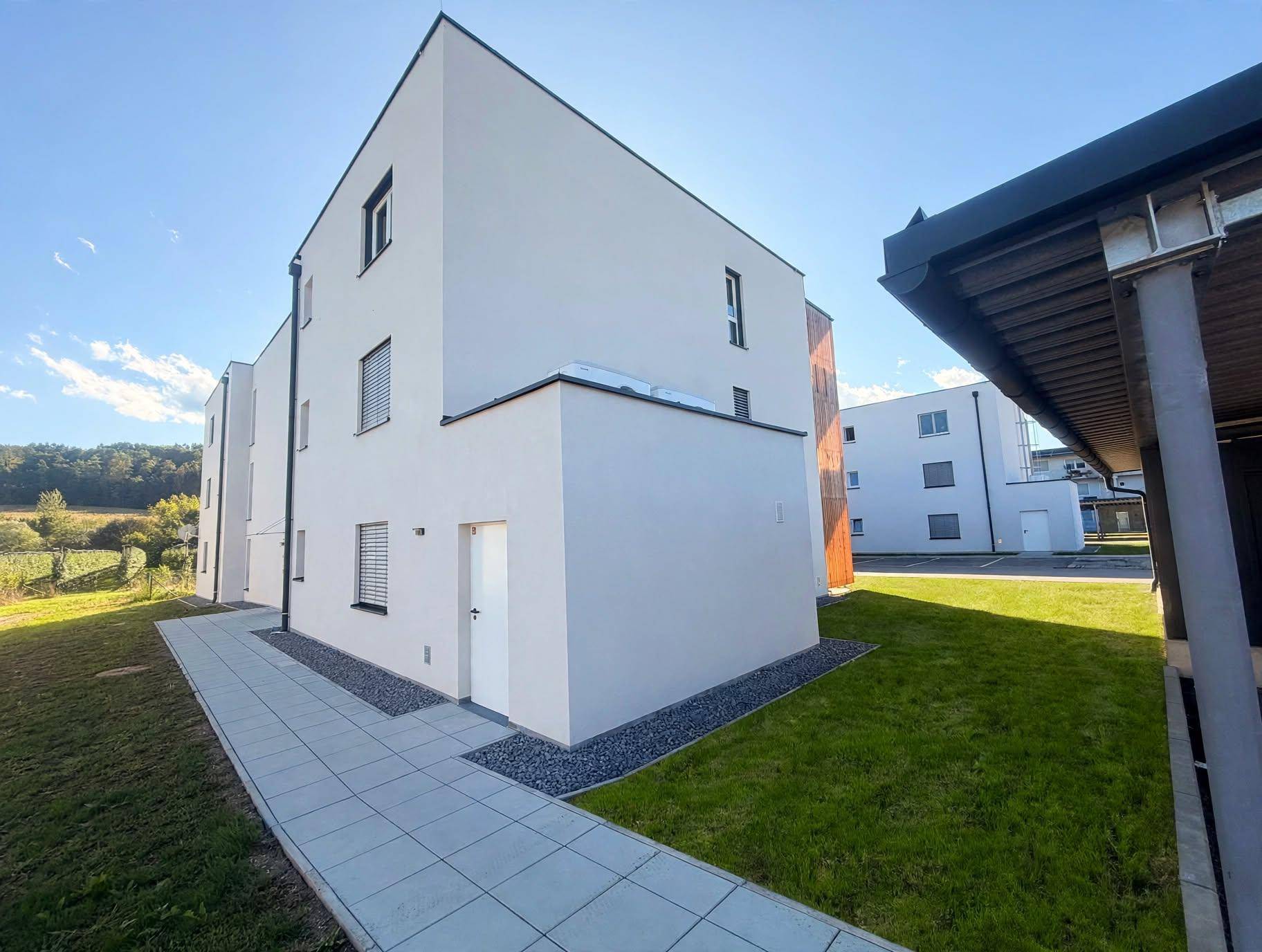 Seitenansicht eines modernen Neubaus mit weißer Fassade, Fenstern und Grünflächen.