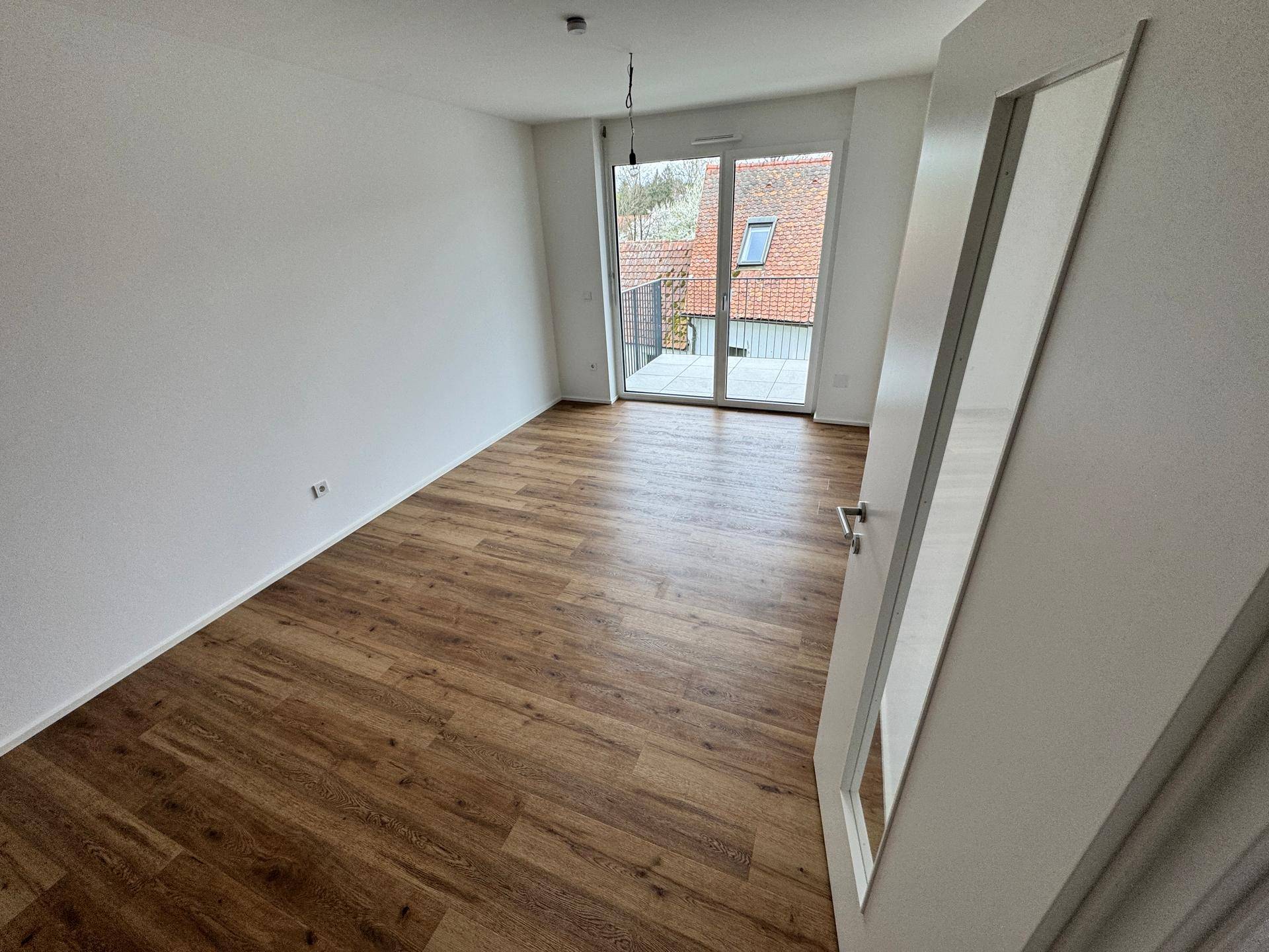 Wohnzimmer mit Holzboden und großer Schiebetür, die direkten Zugang zum Balkon bietet.