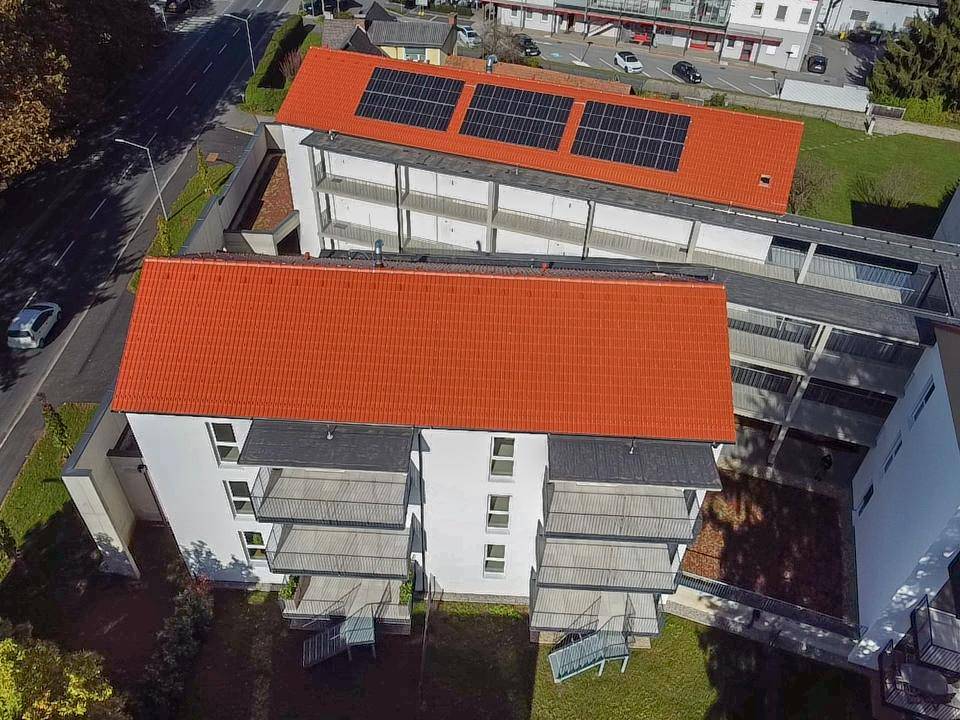 Luftaufnahme von Wohngebäuden mit roten Dächern, Balkonen und Photovoltaikanlagen.