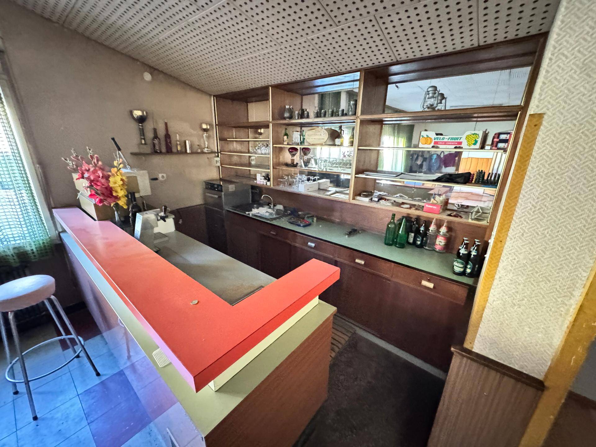 Bar mit roter Theke, Holzregalen und Spiegeln, ausgestattet für gesellige Abende.
