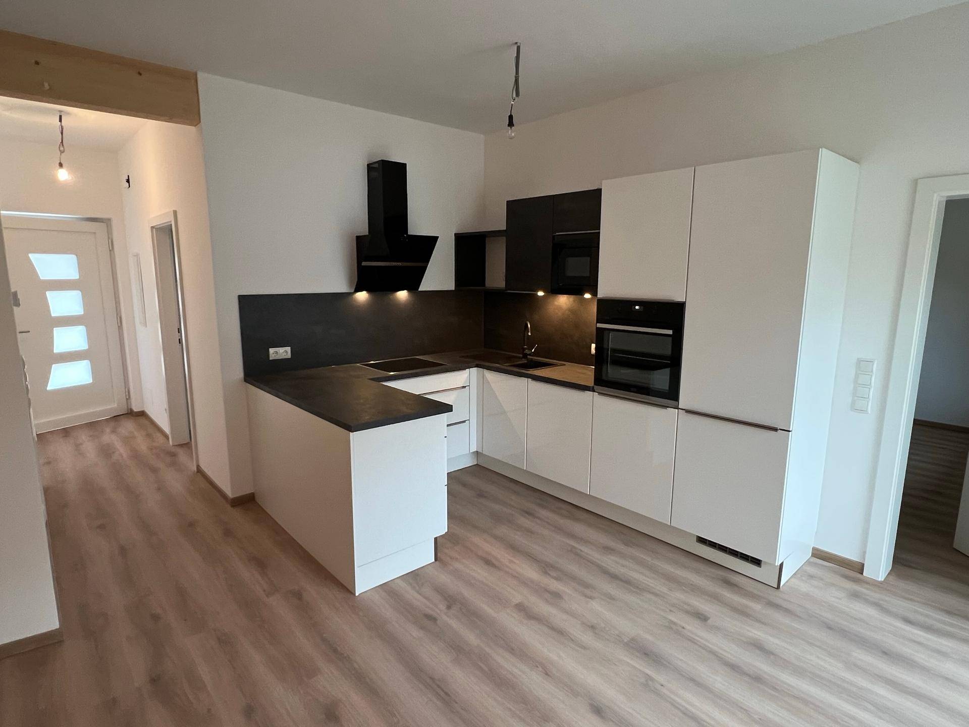Offener Wohnbereich mit moderner Einbauküche und Laminatboden, vom Eingang aus gesehen.