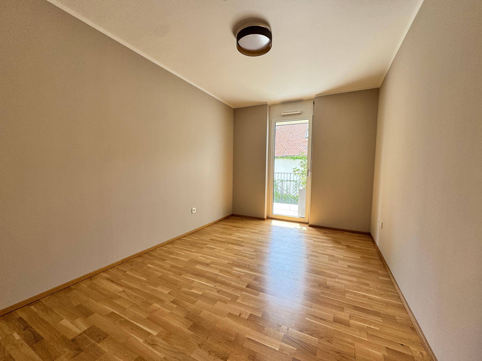 Leeres Schlafzimmer mit Holzparkettboden und Zugang zu einem Balkon oder einer Terrasse.