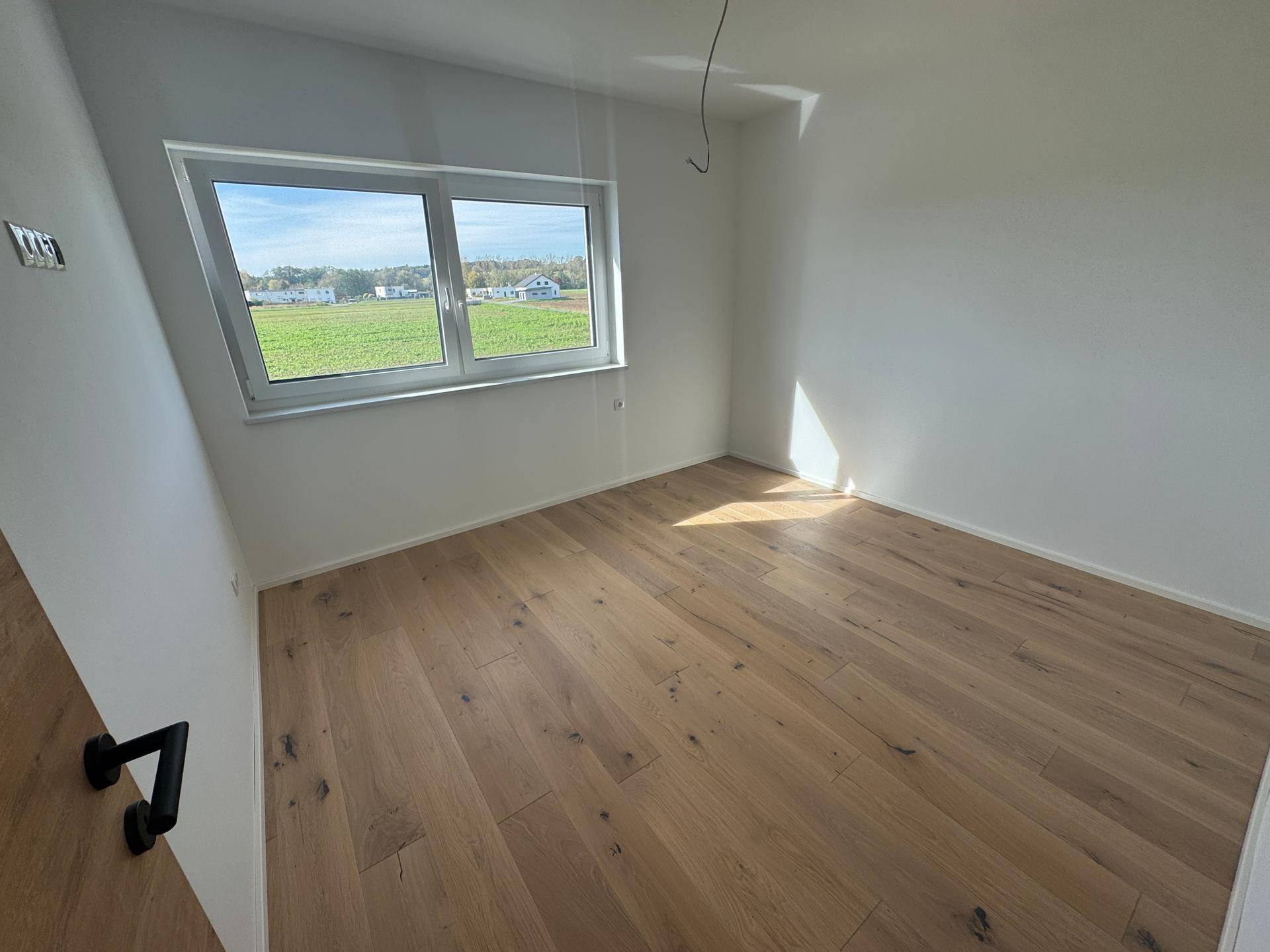 Helles Schlafzimmer mit Eichenparkett, weißen Wänden und Blick ins Grüne.