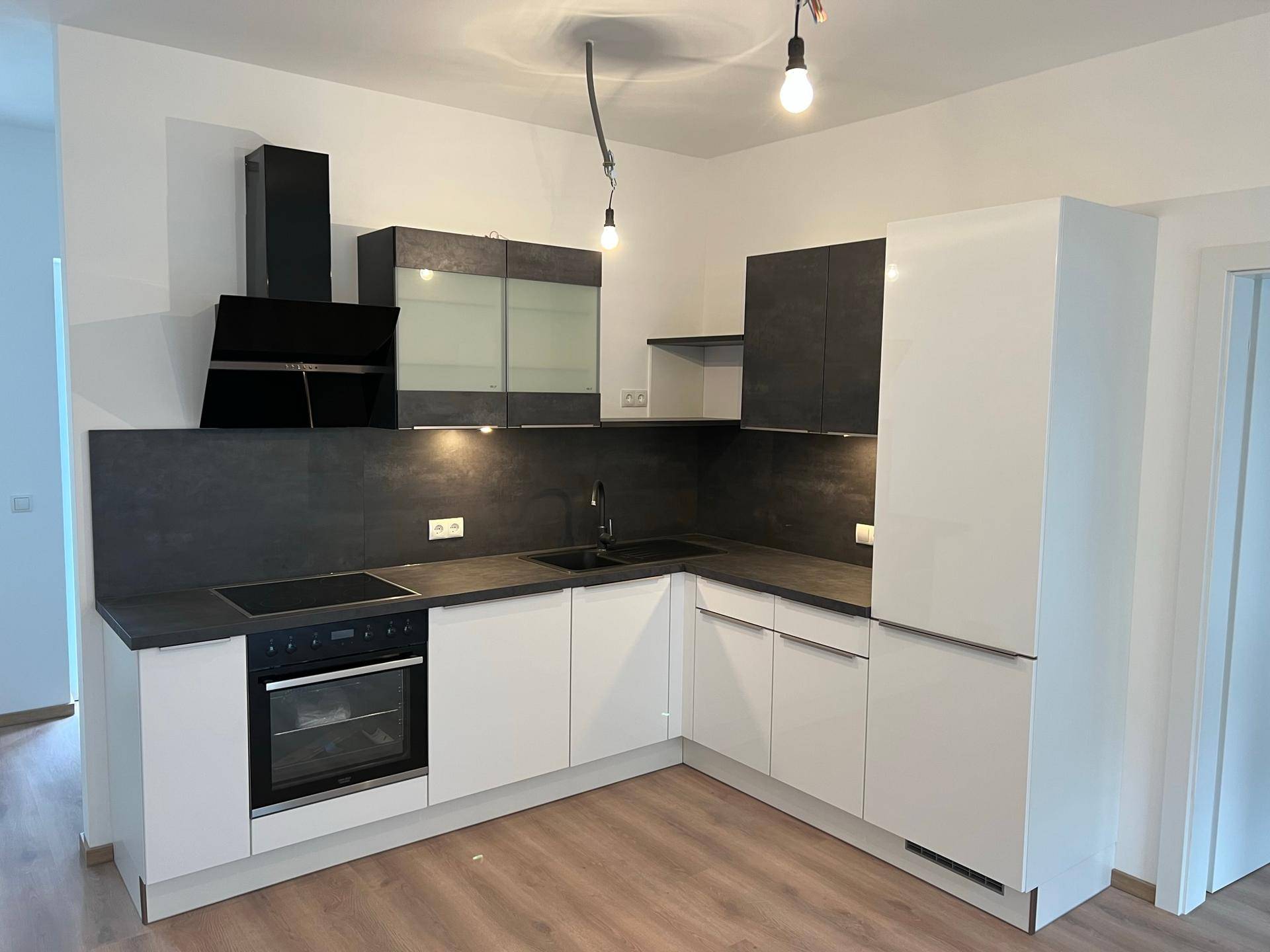 Moderne Einbauküche mit weißen Hochglanzschränken, dunklen Arbeitsplatten und integrierten Geräten.