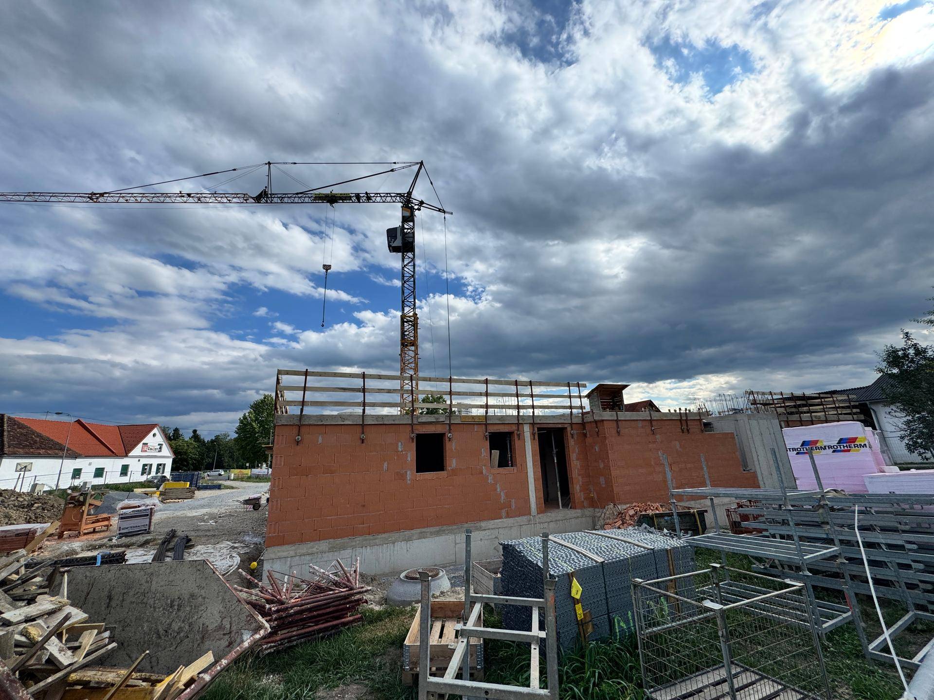 Baustelle mit im Bau befindlichem Gebäude, Ziegelwänden und einem Baukran unter bewölktem Himmel.