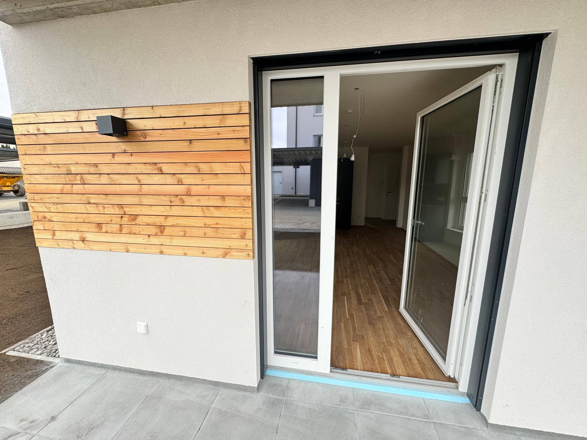Zugang zur Terrasse vom Innenbereich, mit Holzverkleidung an der Fassade des Neubaus.