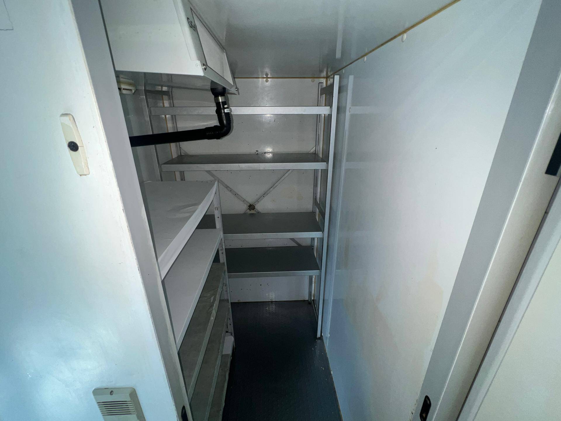 Schmaler Lagerraum mit weißen Regalen und dunklem Boden, ideal für Vorräte.