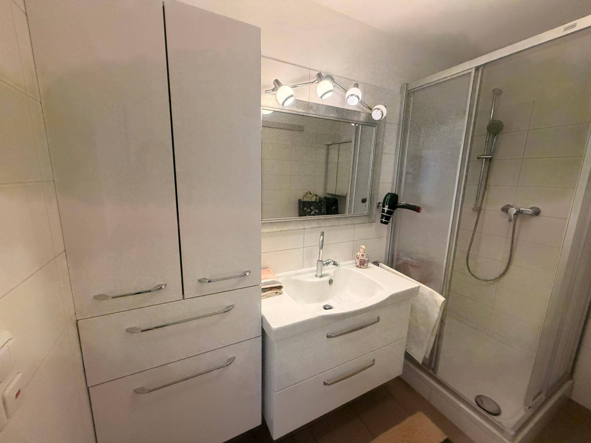 Helles Badezimmer mit Duschkabine, modernem Waschbecken und Spiegelschrank.