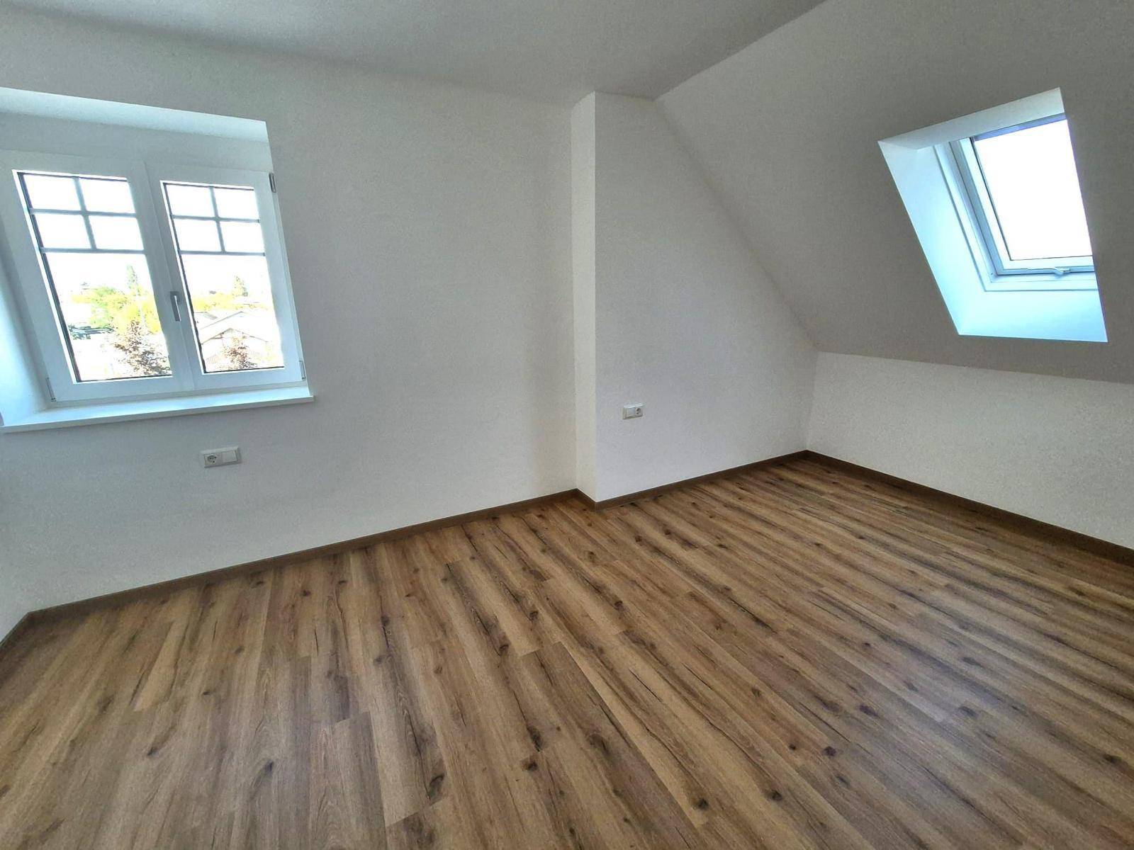 Helles Zimmer im Dachgeschoss mit Laminatboden, Dachfenster und Gaubenfenster.