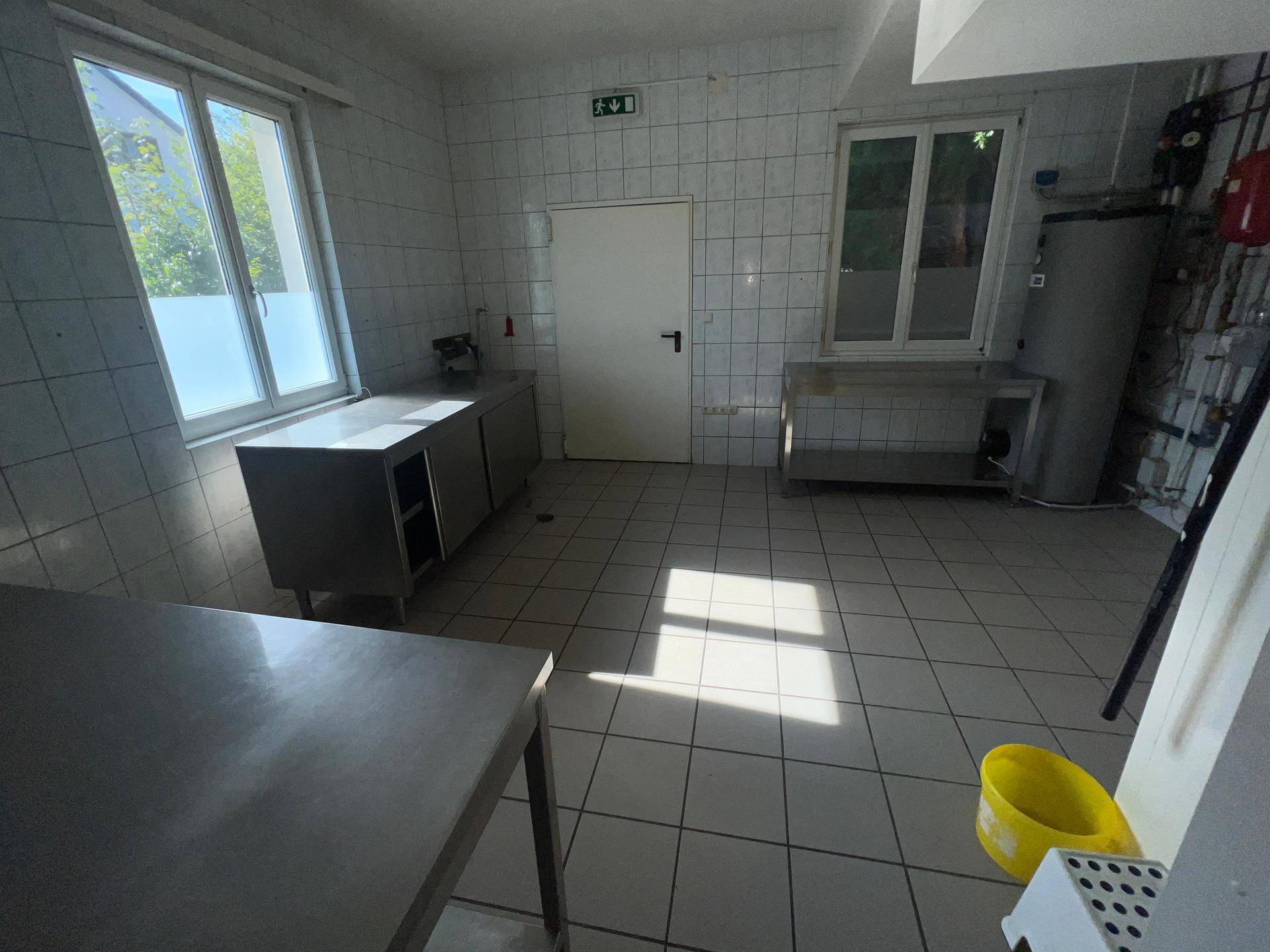 Gewerbliche Küche mit Edelstahlmöbeln, gefliesten Wänden und Fenstern für natürliches Licht.