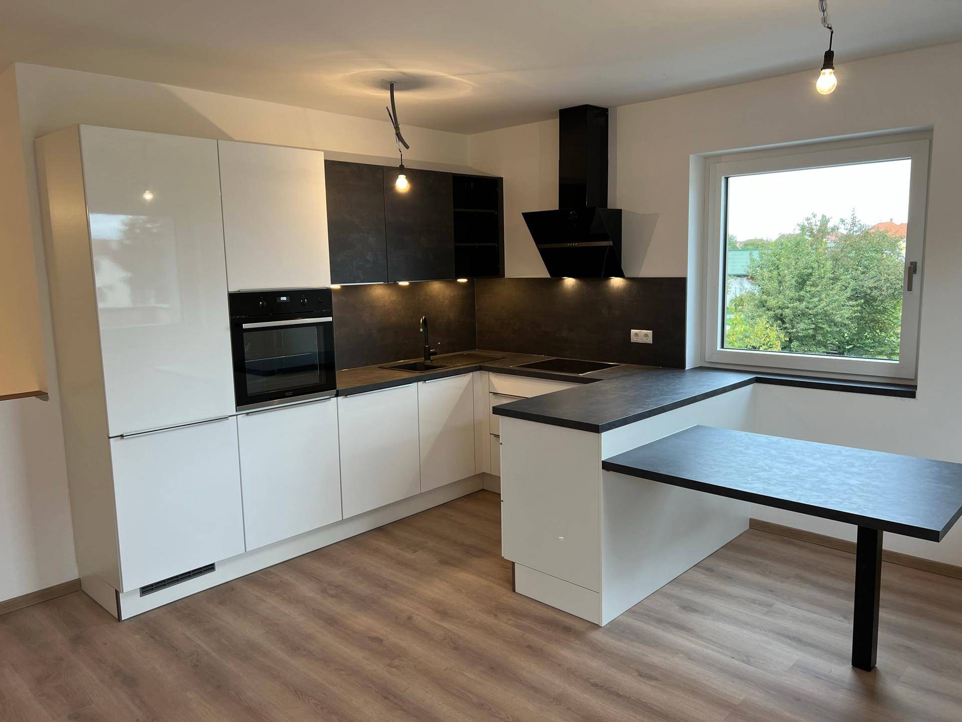 Moderne Einbauküche mit weißen und anthrazitfarbenen Schränken, ausgestattet mit neuen Geräten und Fenster.