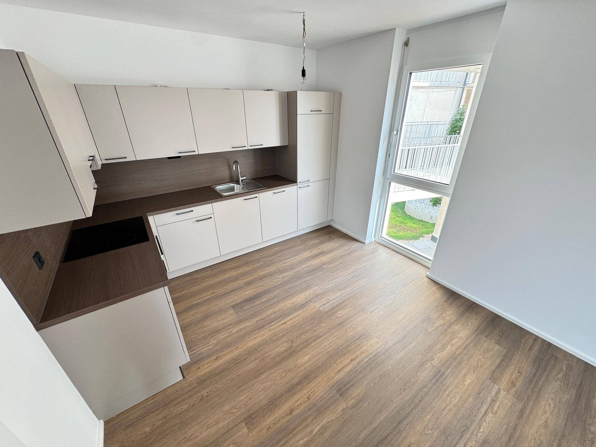 Moderne Einbauküche mit hellen Schränken, dunkler Arbeitsplatte und großem Fenster mit Blick ins Grüne.