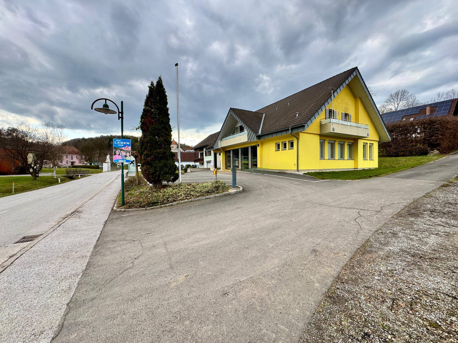 Gelbes Gebäude mit Satteldach und Parkplatz an einer ländlichen Straße.