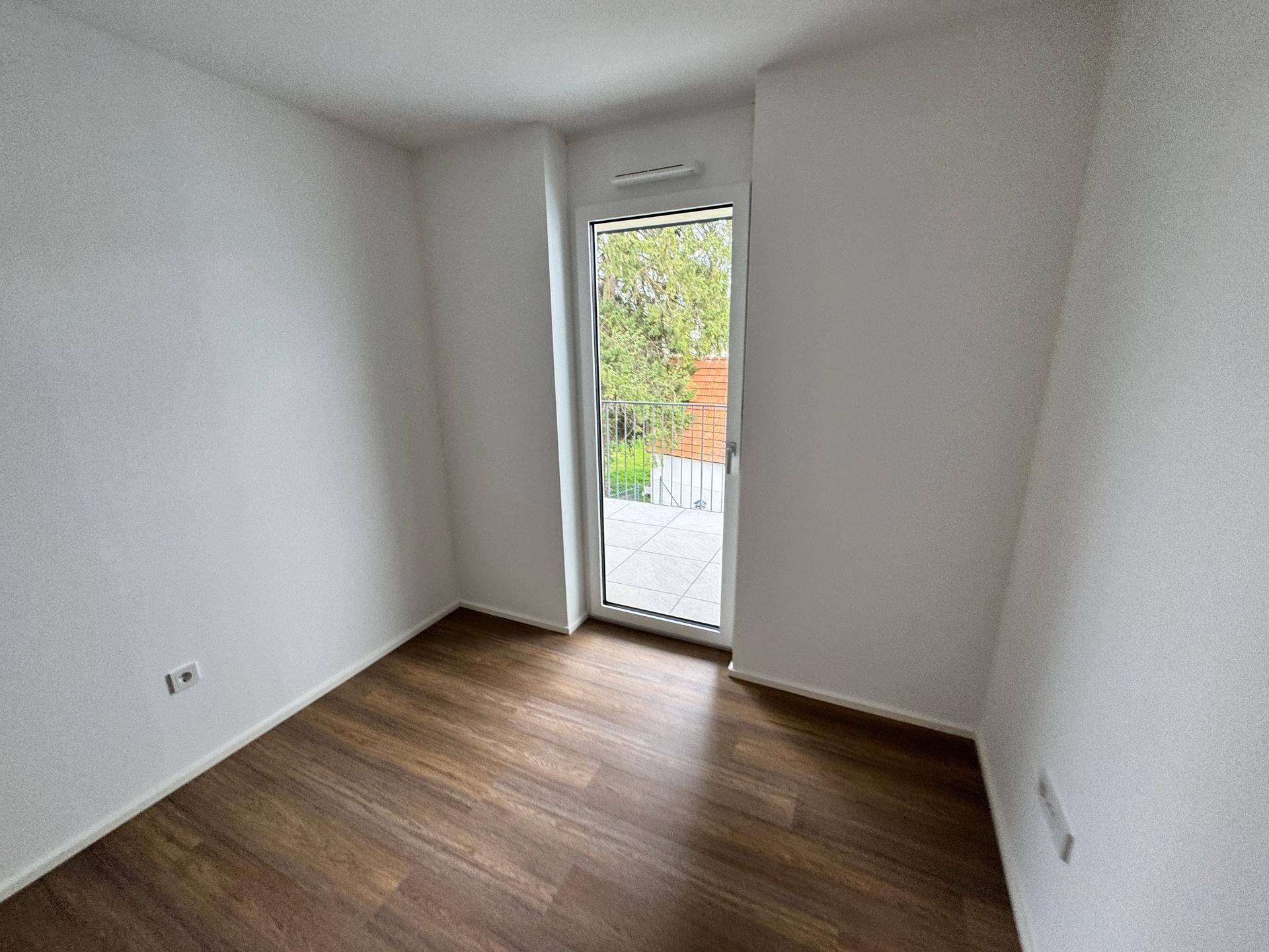Helles Schlafzimmer mit Laminatboden und Zugang zu einem französischen Balkon.
