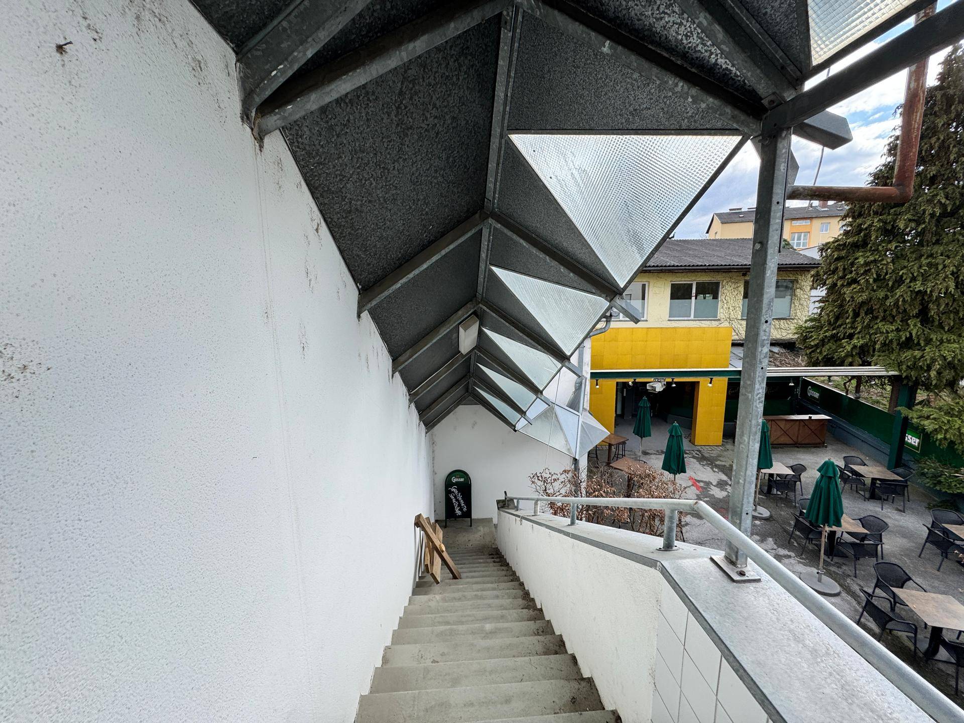 Außentreppe mit Metallgeländer und Überdachung, die zu einem Café-Eingang führt.