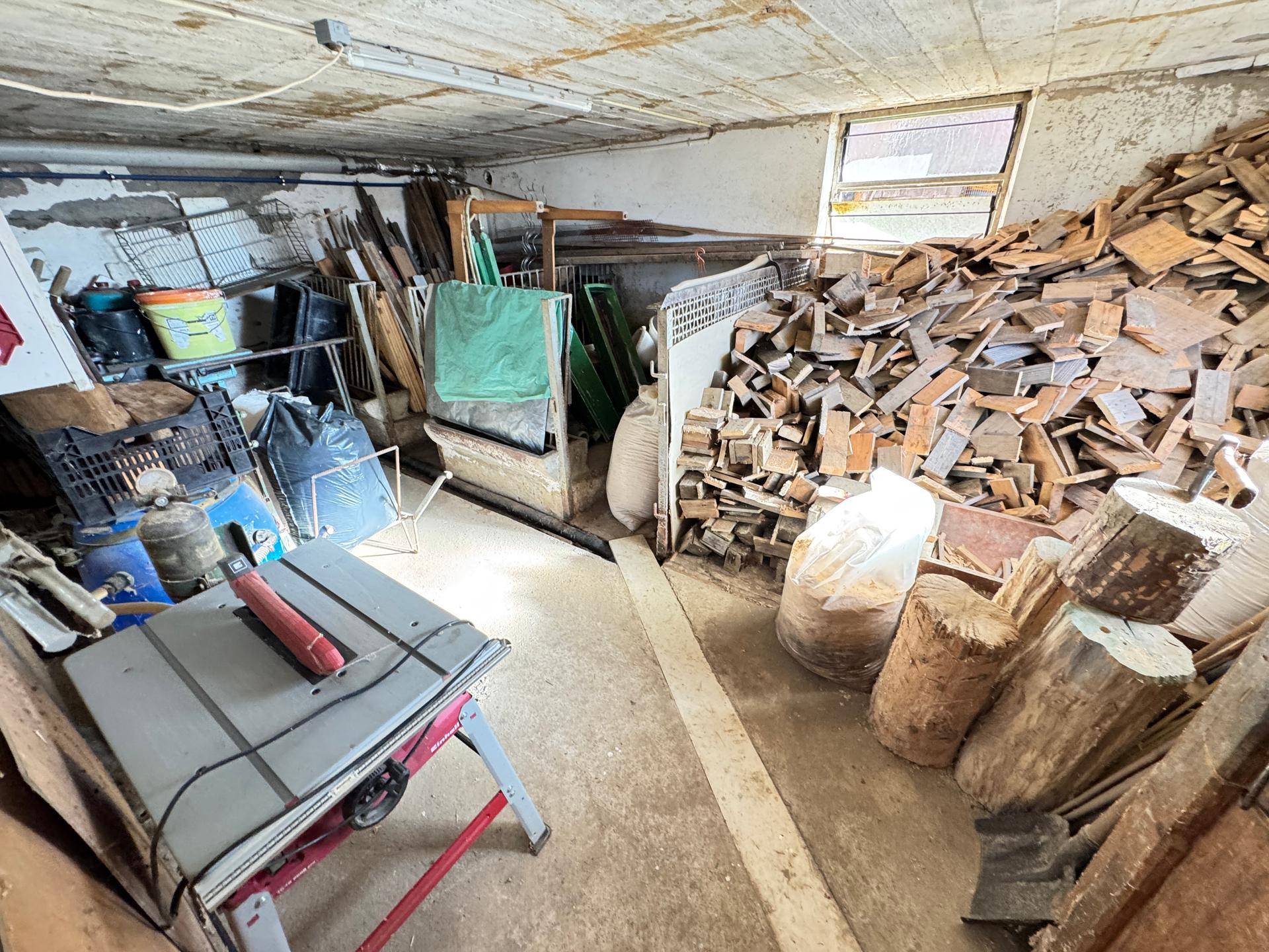Kellerraum mit Holzstapeln und Werkzeugen, ideal als Lager oder Werkstatt.