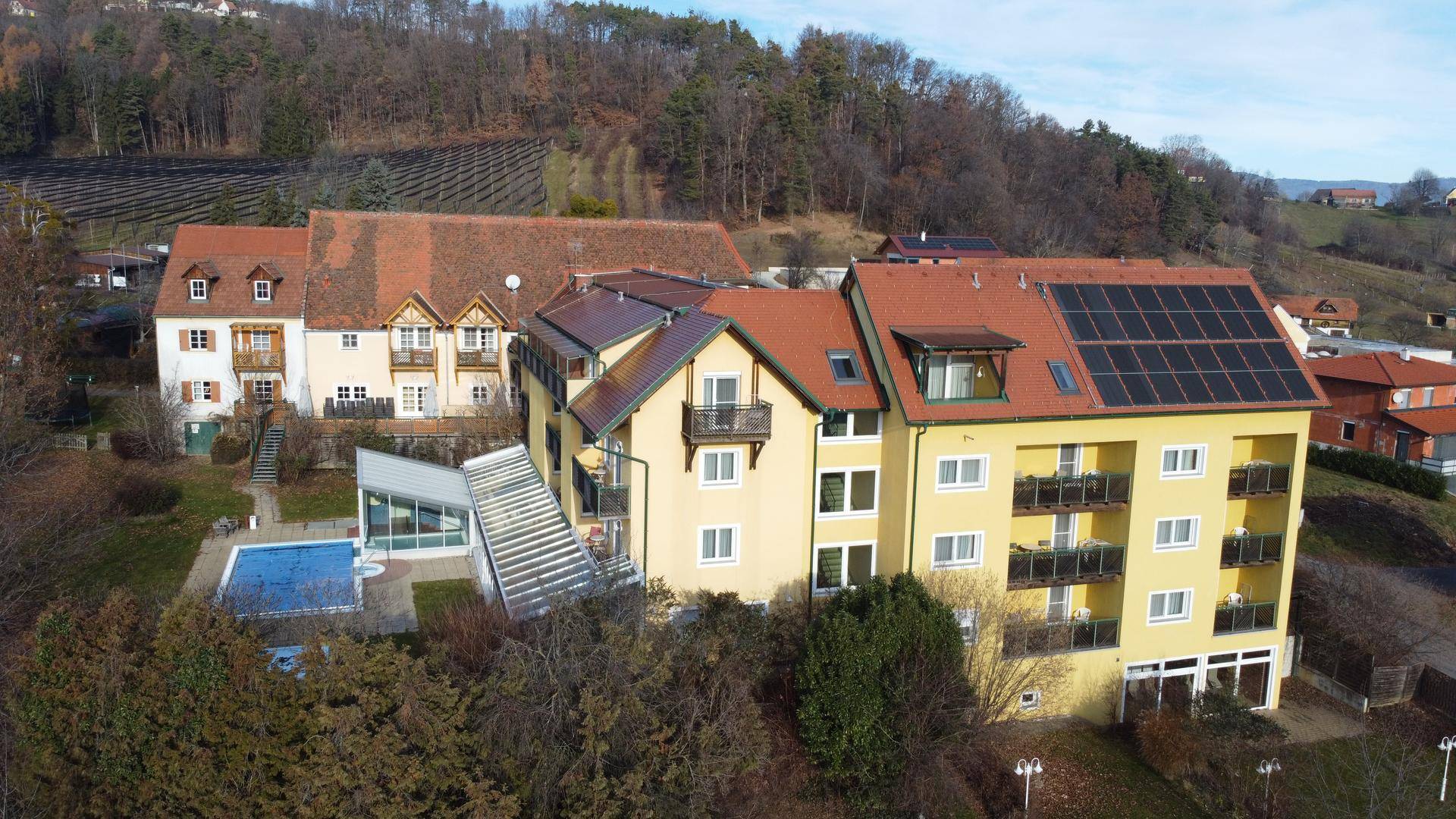 Luftaufnahme des Gebäudekomplexes mit Außenpool, Solaranlagen und umliegender Natur.