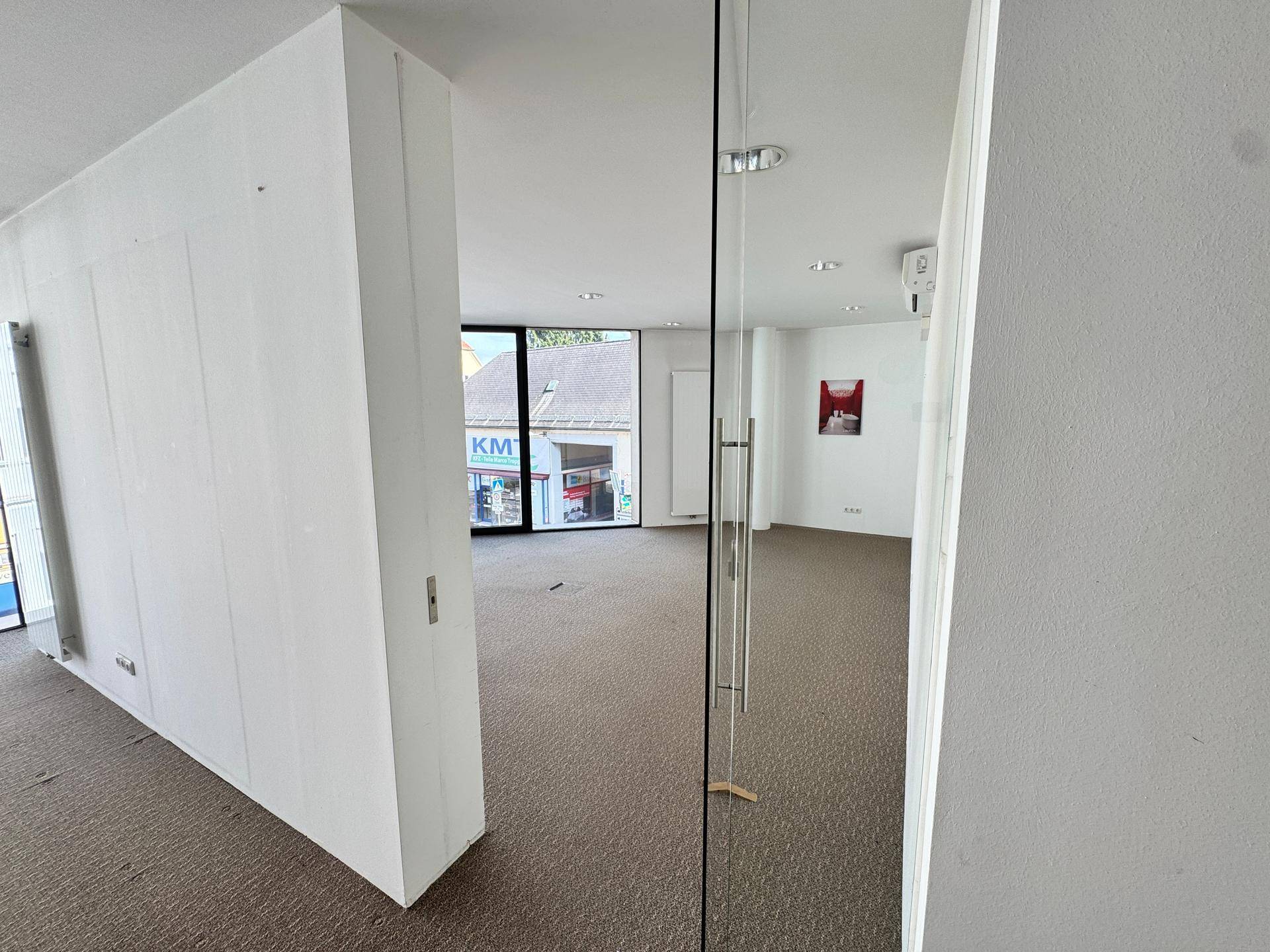 Innenraum mit Teppichboden, Glaswand und Blick auf die umliegende Bebauung.