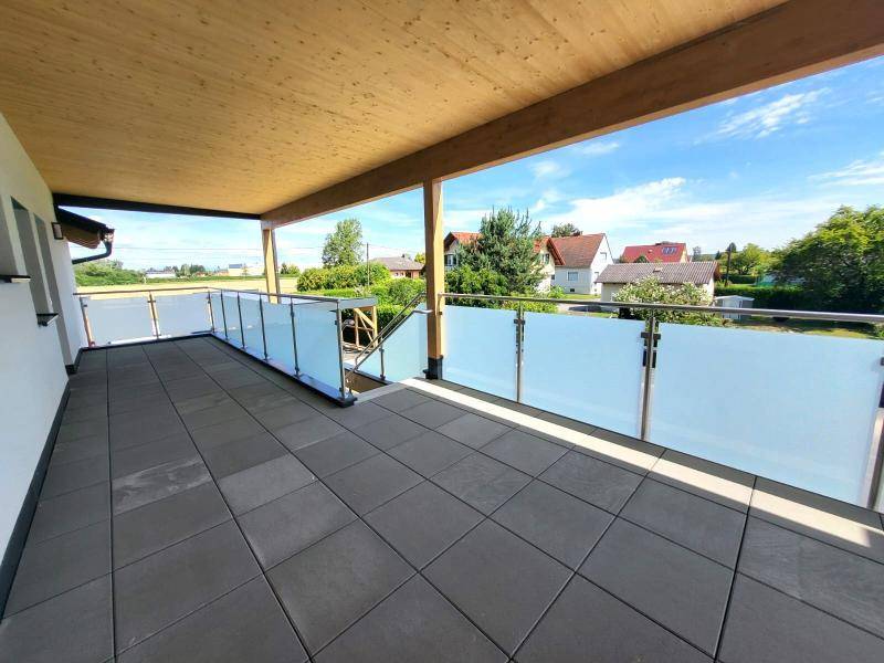 Großer Balkon mit Fliesenboden, Glasgeländer und weitem Blick auf die Nachbarschaft.
