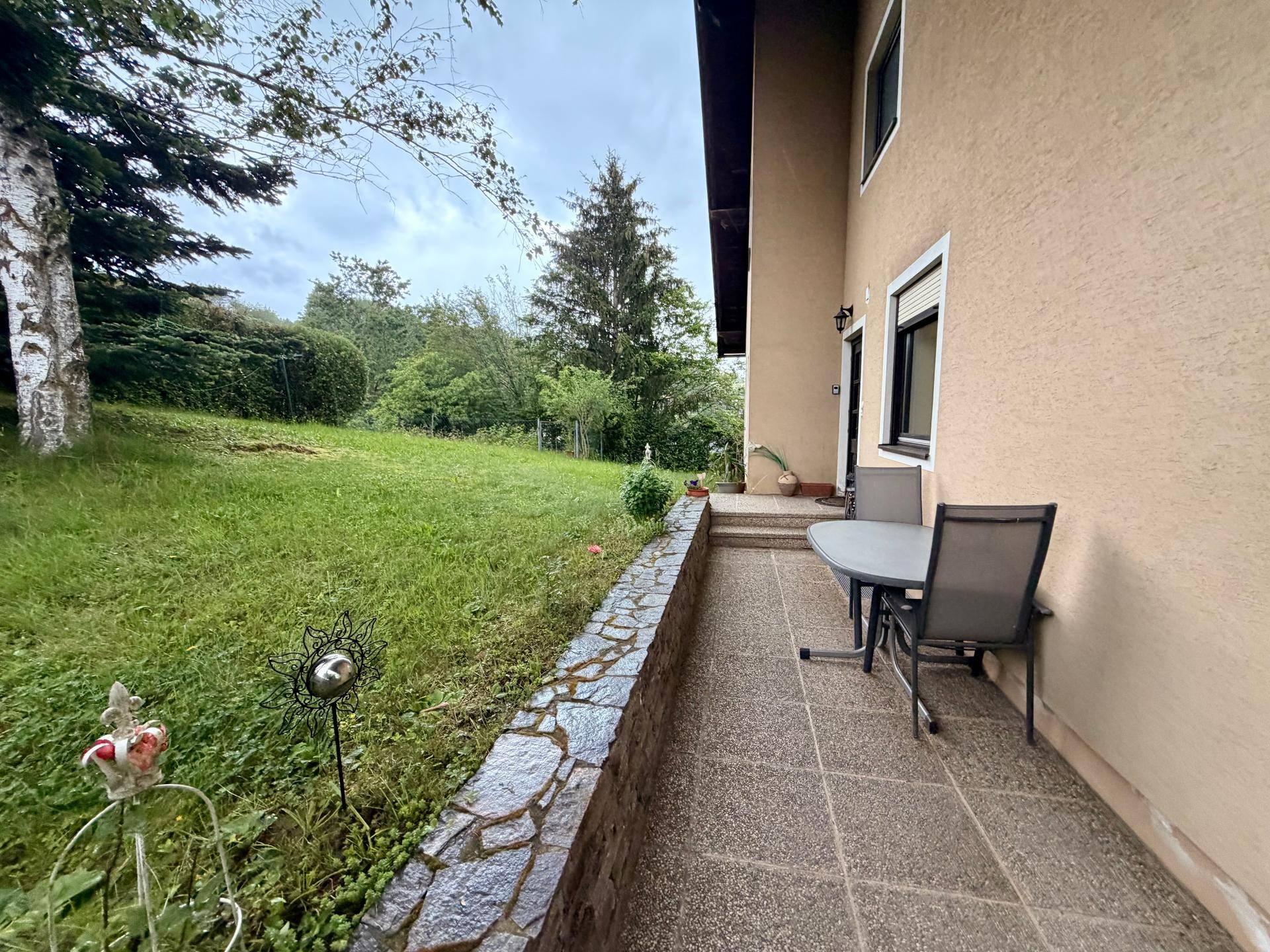 Gepflasterte Terrasse mit Gartenmöbeln und Blick auf den Rasen und die Steinmauer.