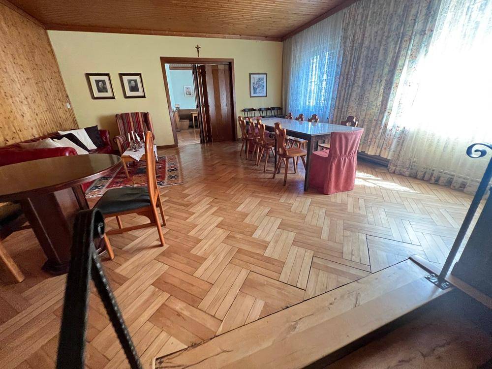 Geräumiger Wohn- und Essbereich mit Fischgrätparkett, Holzvertäfelung und großen Fenstern.